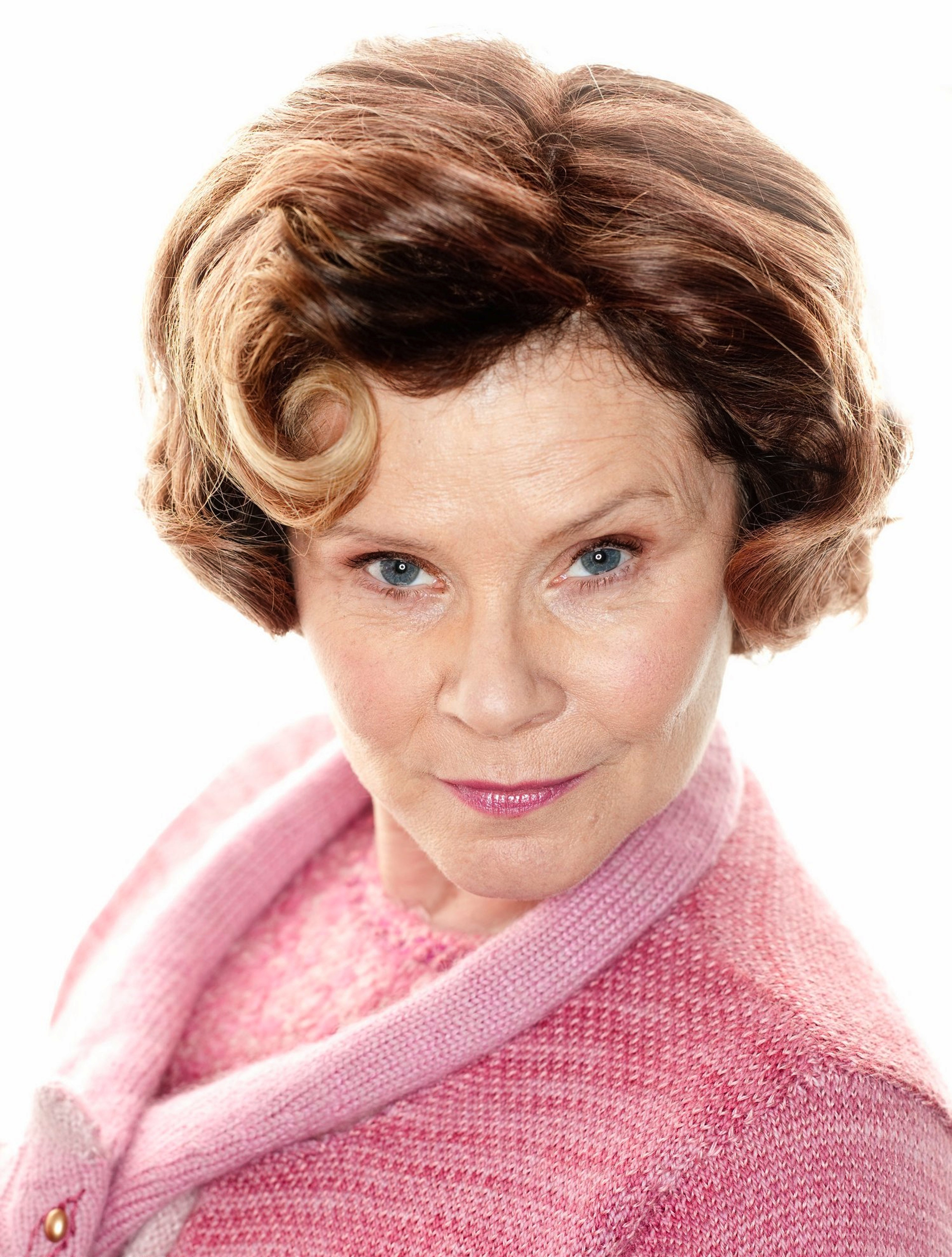 A middle-aged woman with curly brown hair wearing a pink cardigan