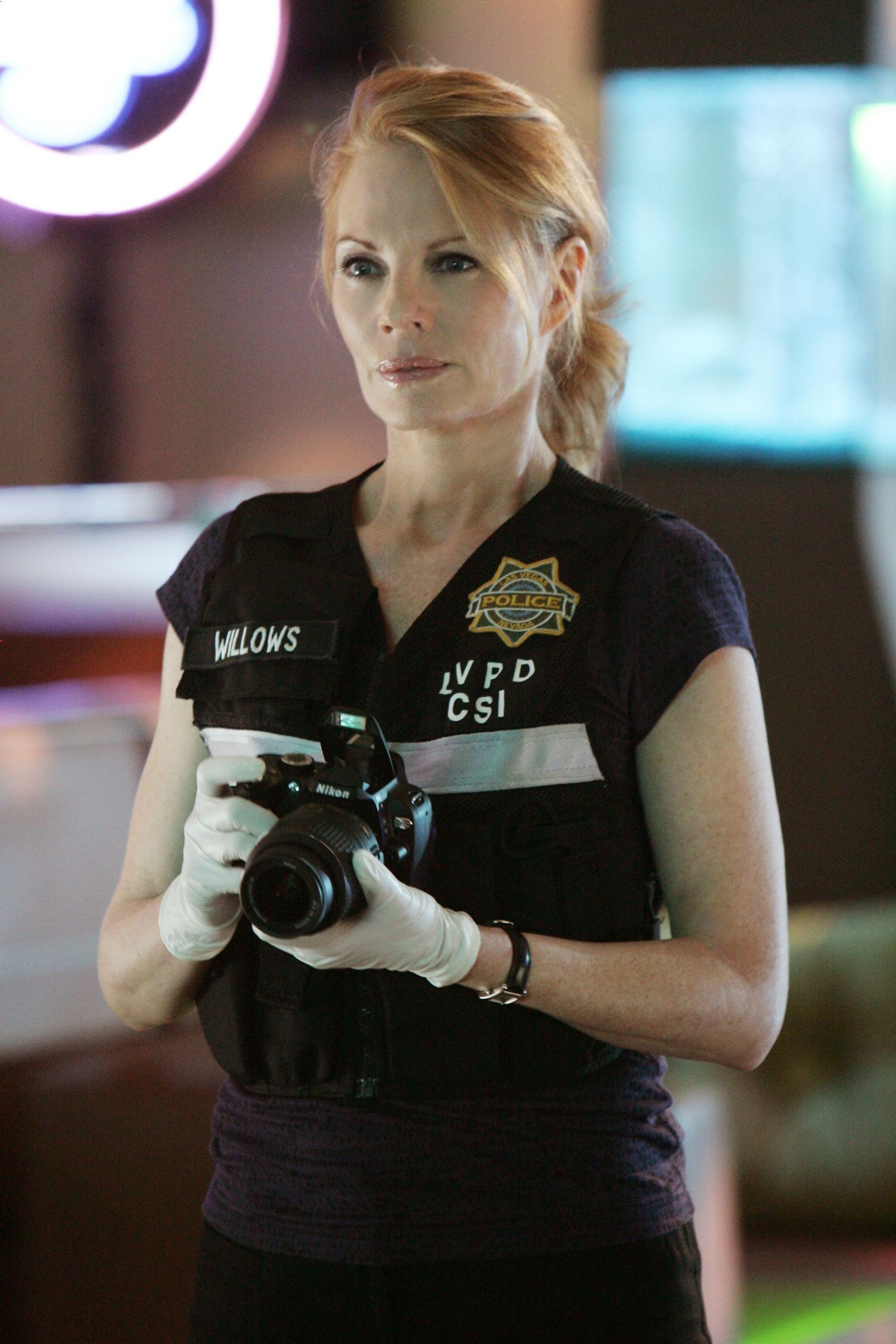 A woman in a black LVPD CSI shirt holding a camera in a professional setting