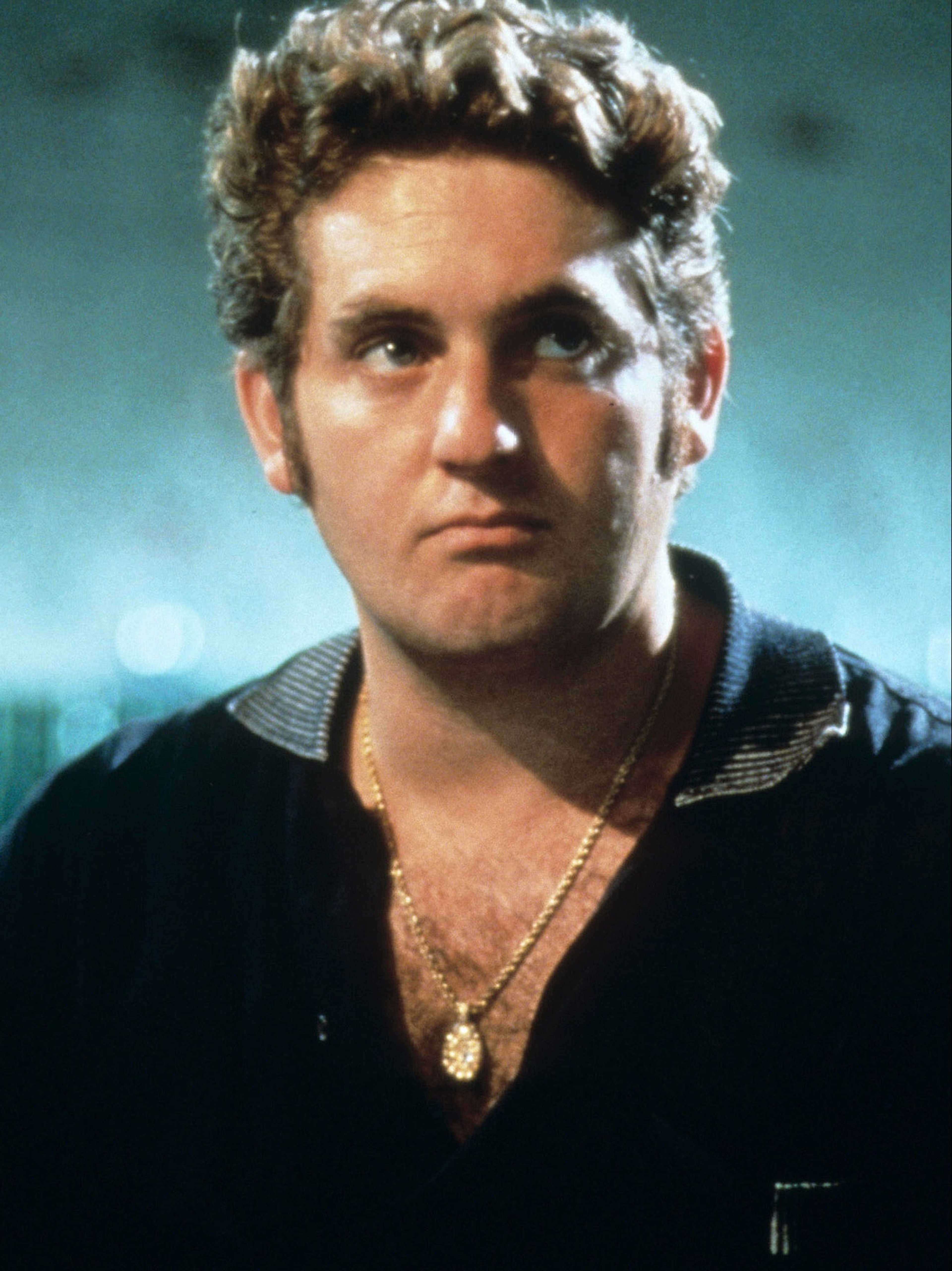A middle-aged man with curly hair and an intense expression, wearing a black jacket.