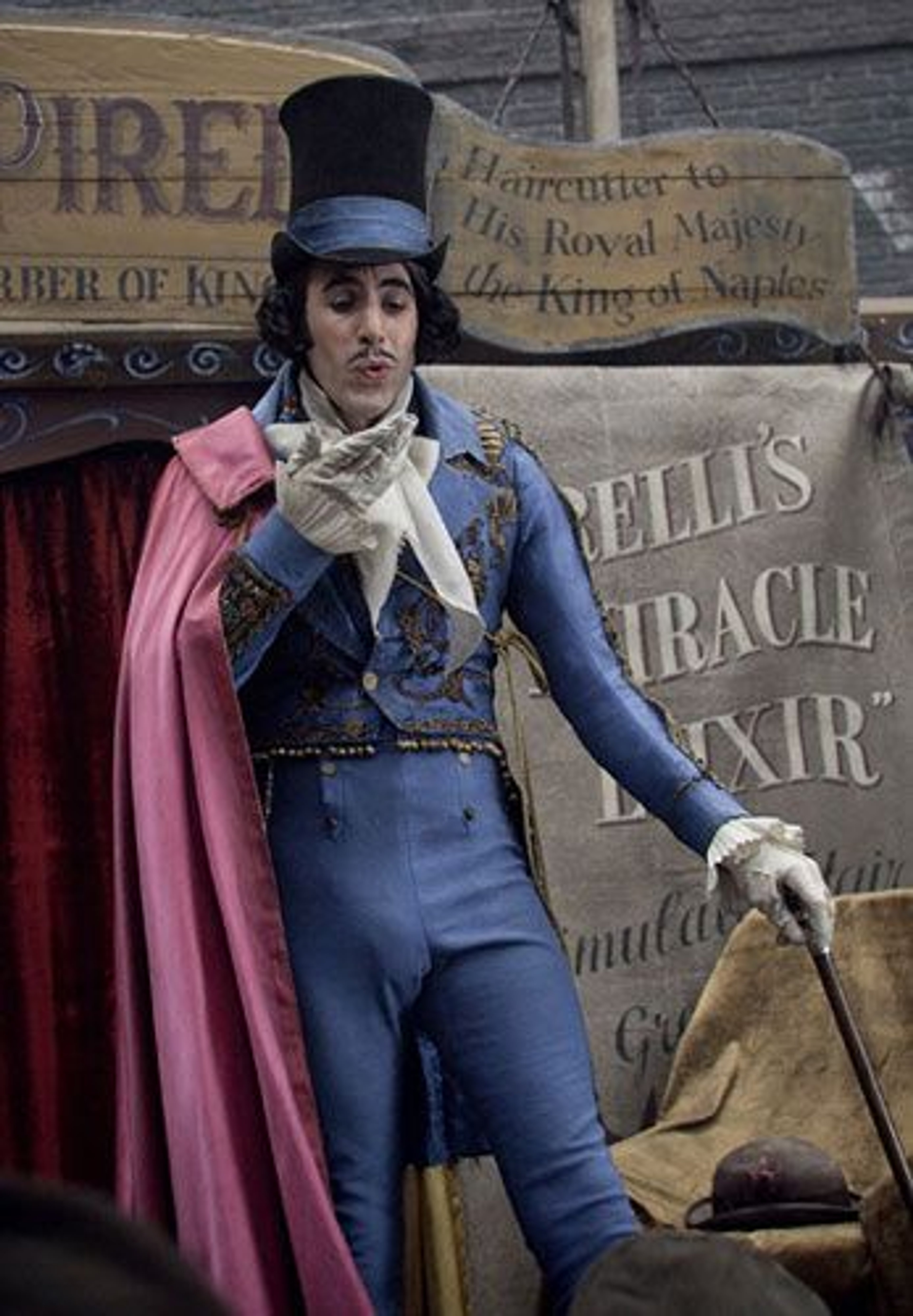 A flamboyant, theatrical-looking man in Victorian-era clothing standing in front of a barber shop sign