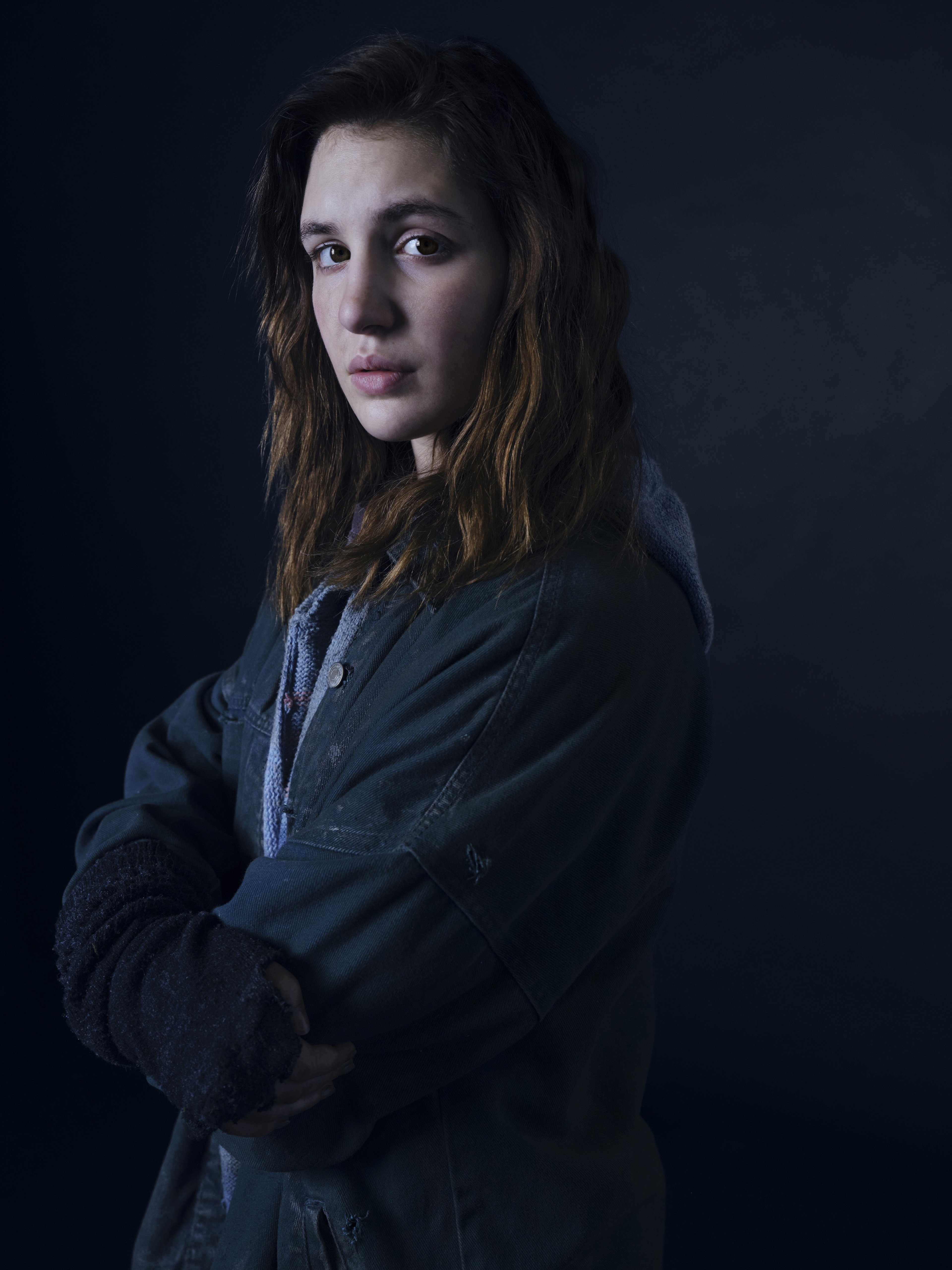 A young woman with dark hair wearing a black jacket, looking serious and pensive.