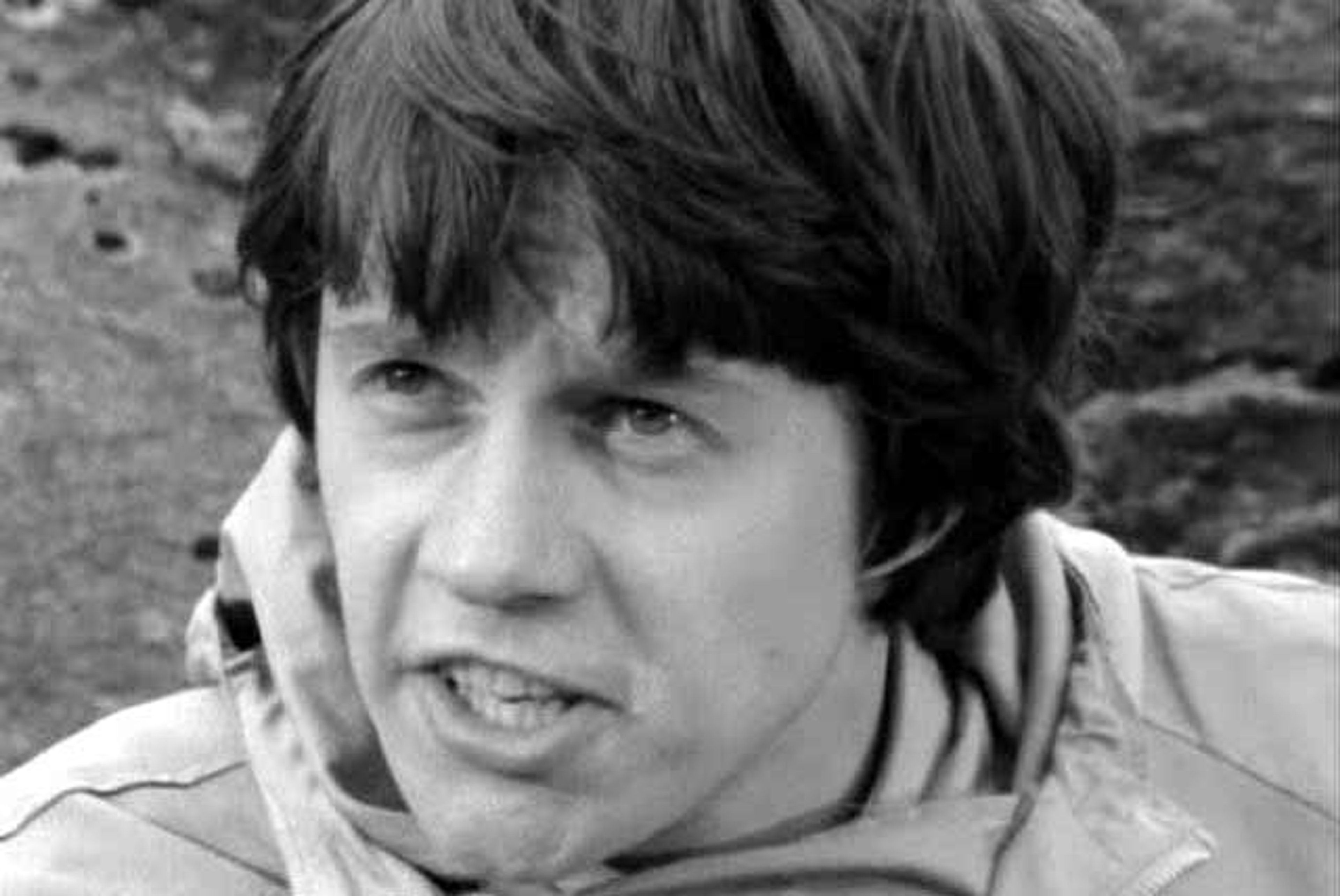 A young man with short dark hair wearing a light-colored shirt or jacket, in a black and white photograph.