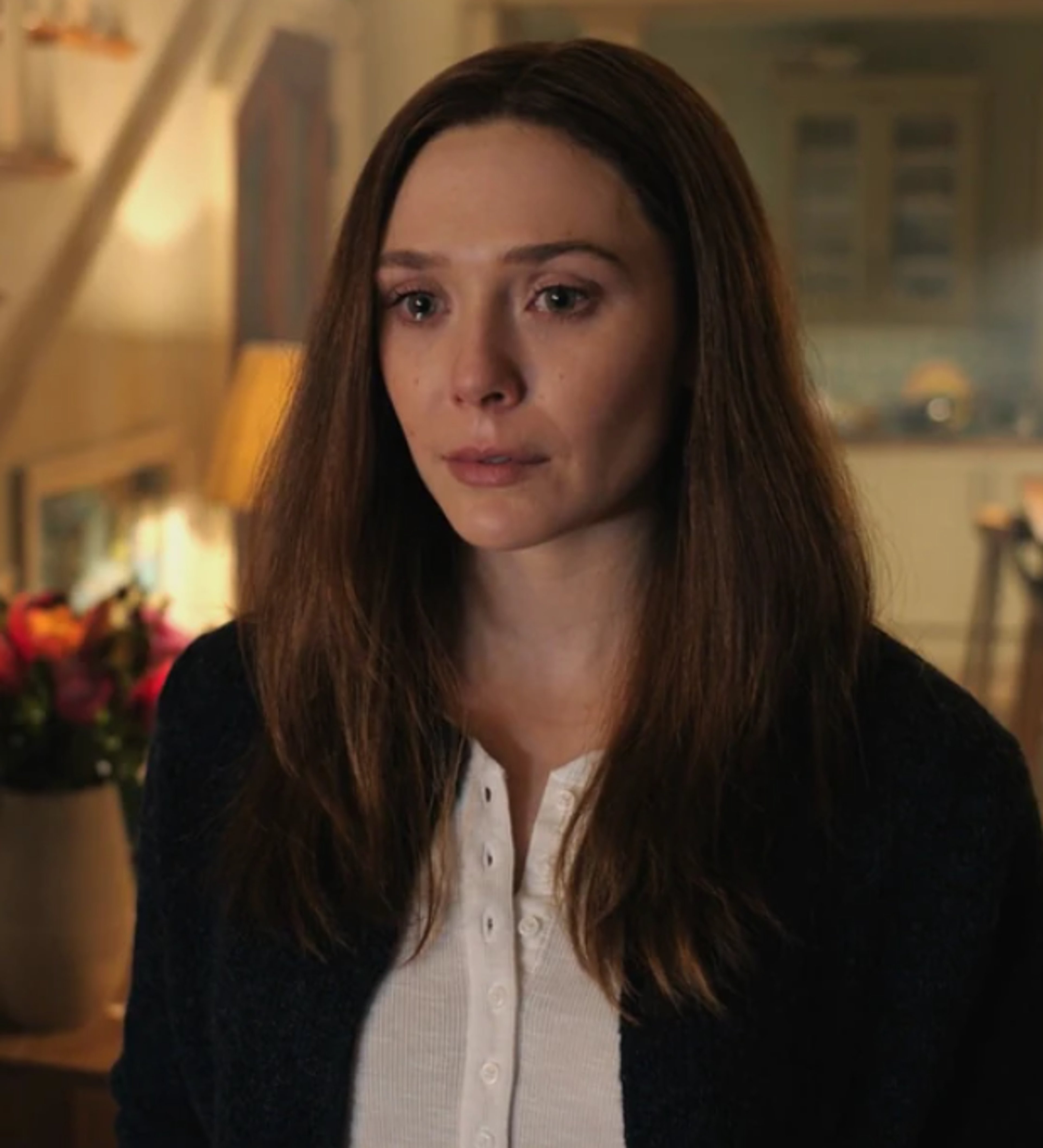 A woman with long brown hair wearing a black jacket, looking serious and contemplative.
