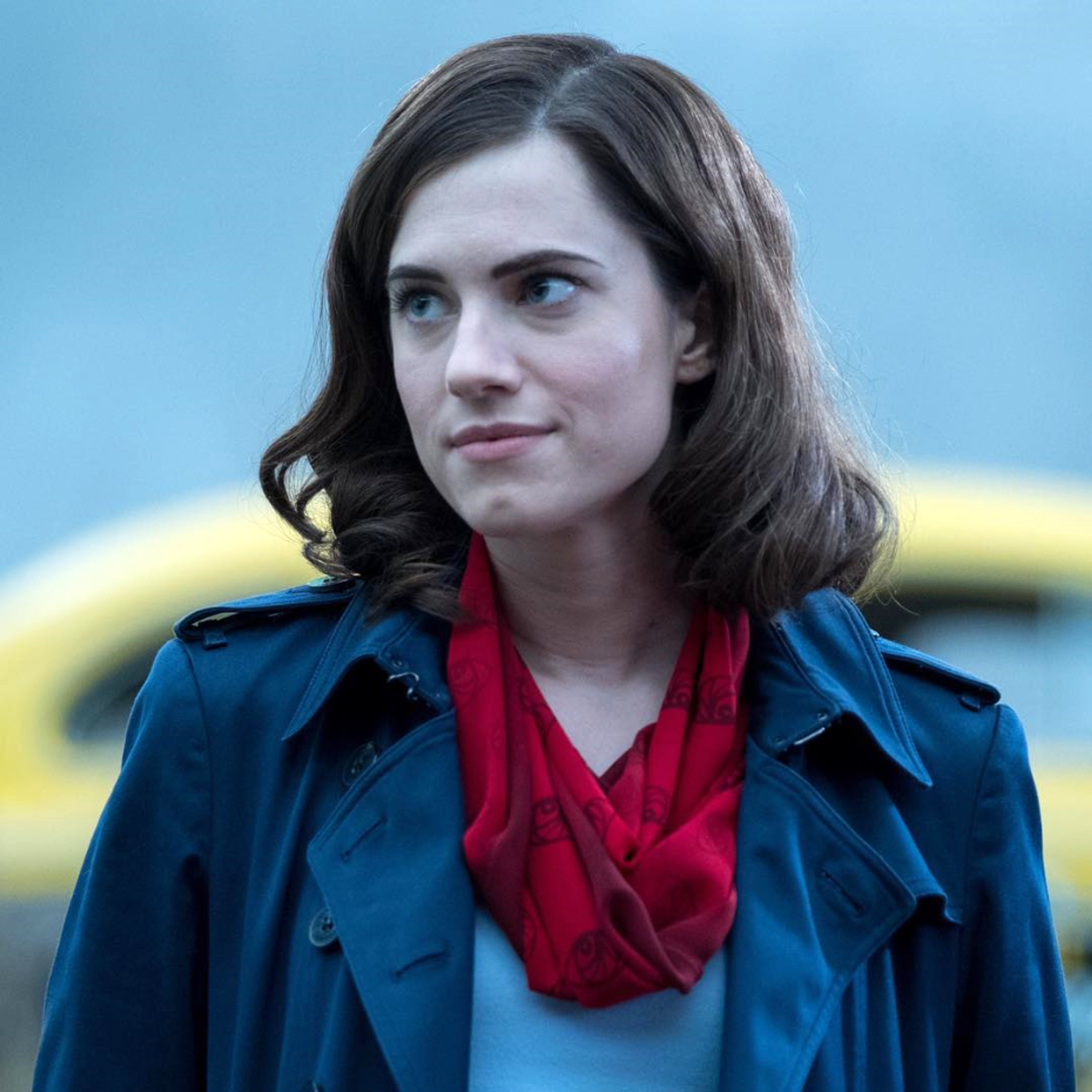 A woman with dark hair wearing a blue coat and red scarf