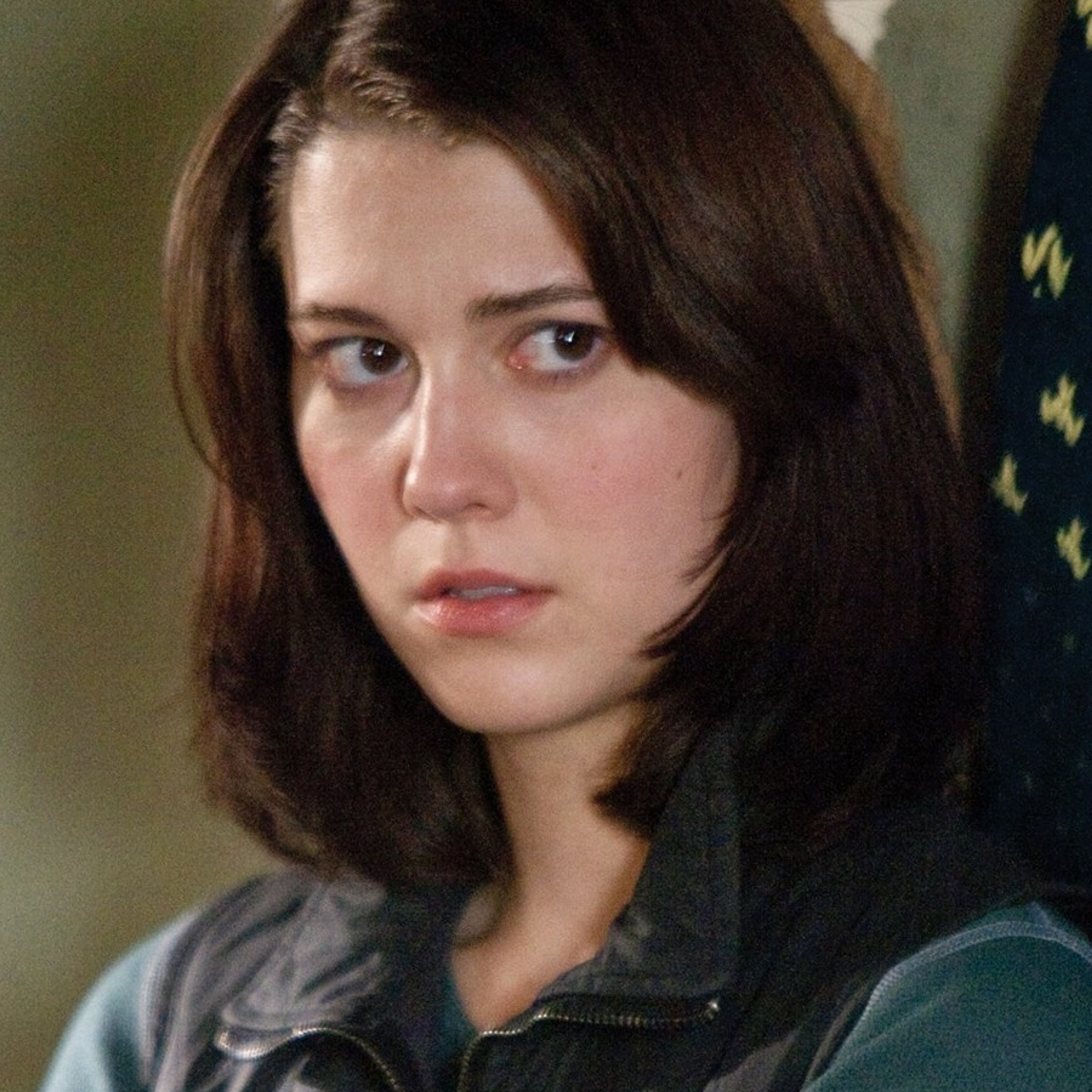 A young woman with dark hair wearing a gray jacket, looking serious and determined.
