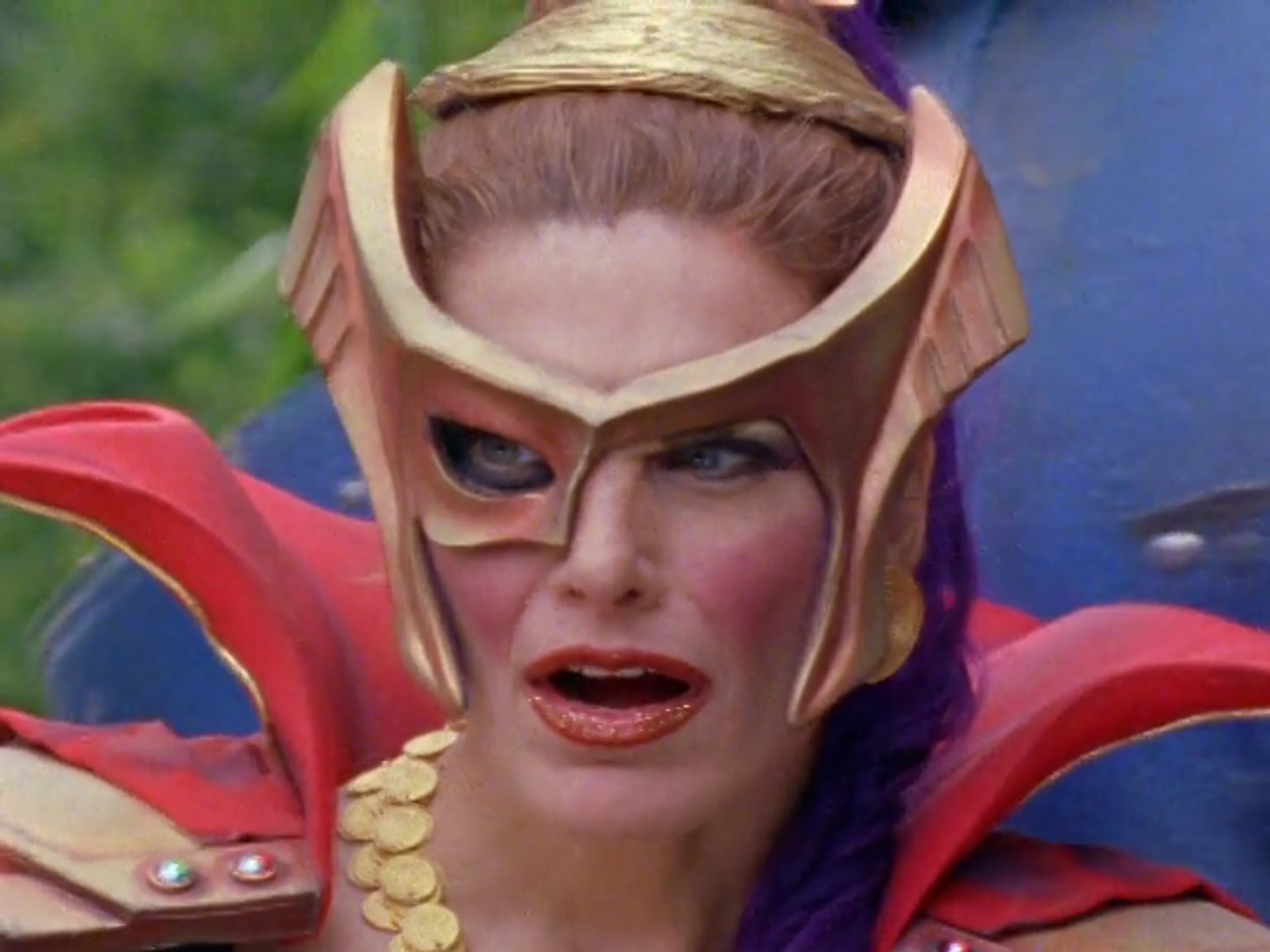 A woman with bright red hair and an elaborate costume, making an intense facial expression.