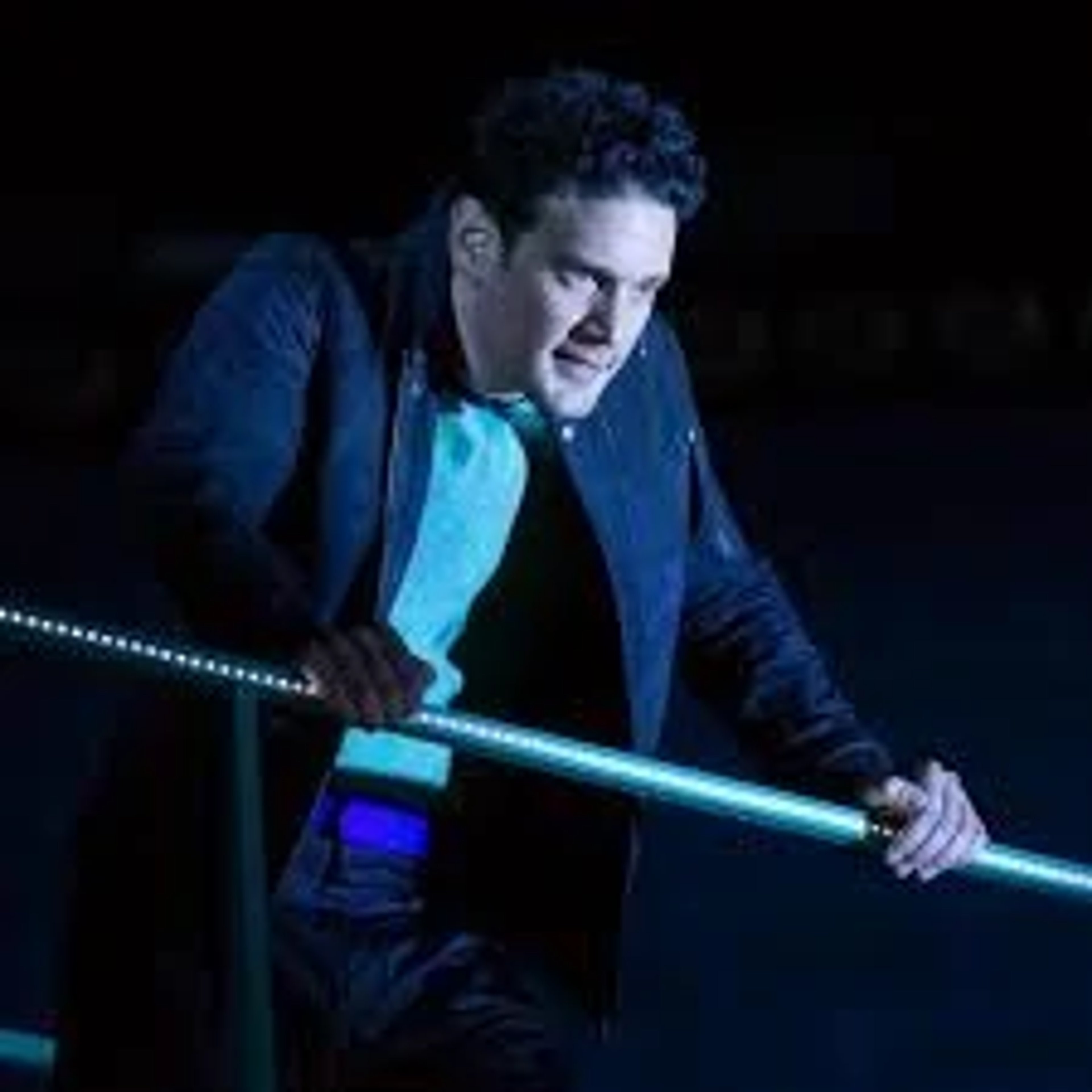 A man in a dark suit standing on a stage or platform with a serious expression