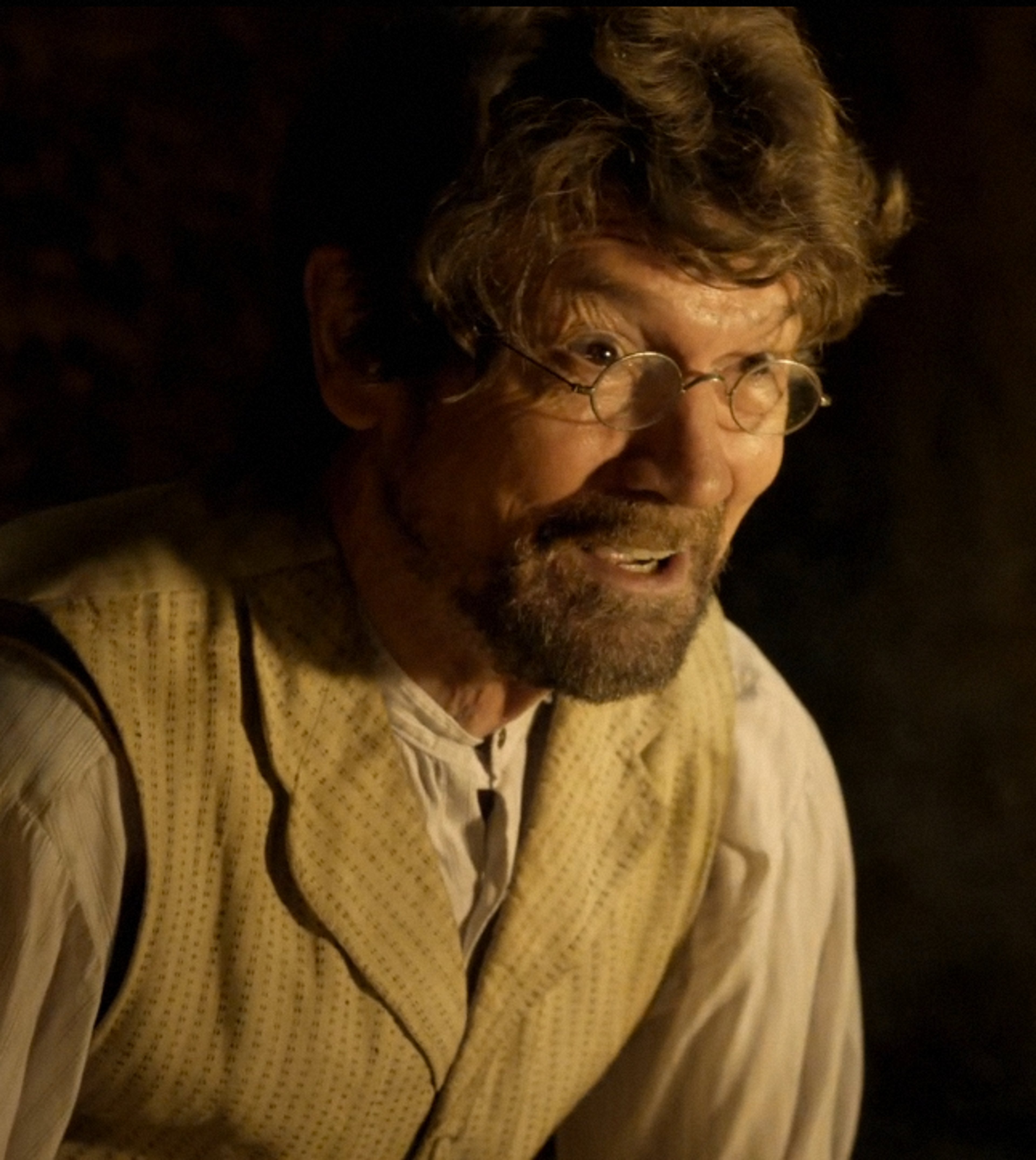 An older man with a gray beard and glasses, wearing a light-colored shirt or jacket