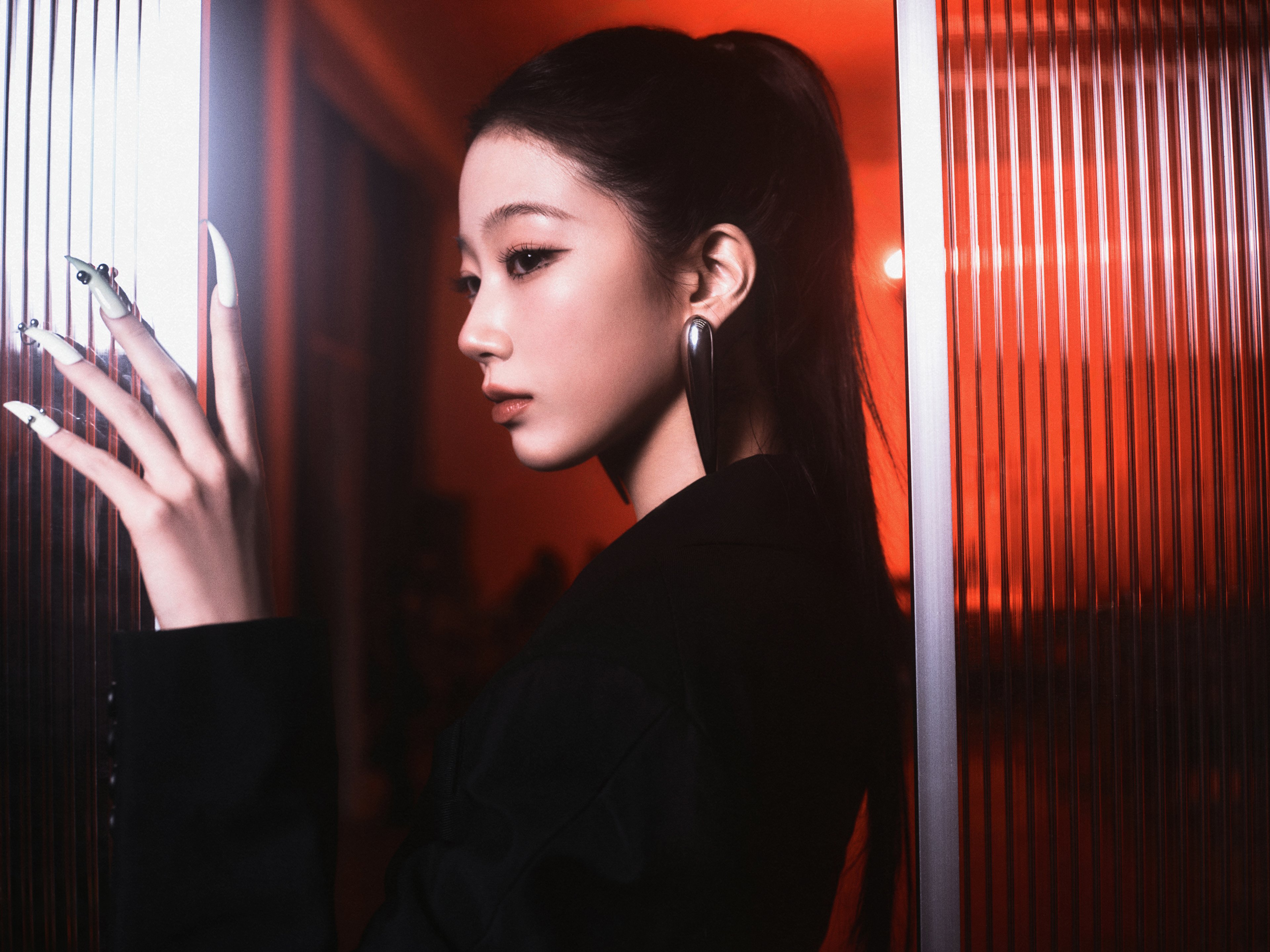 A young woman with long dark hair wearing a black outfit in a dimly lit setting with red lighting