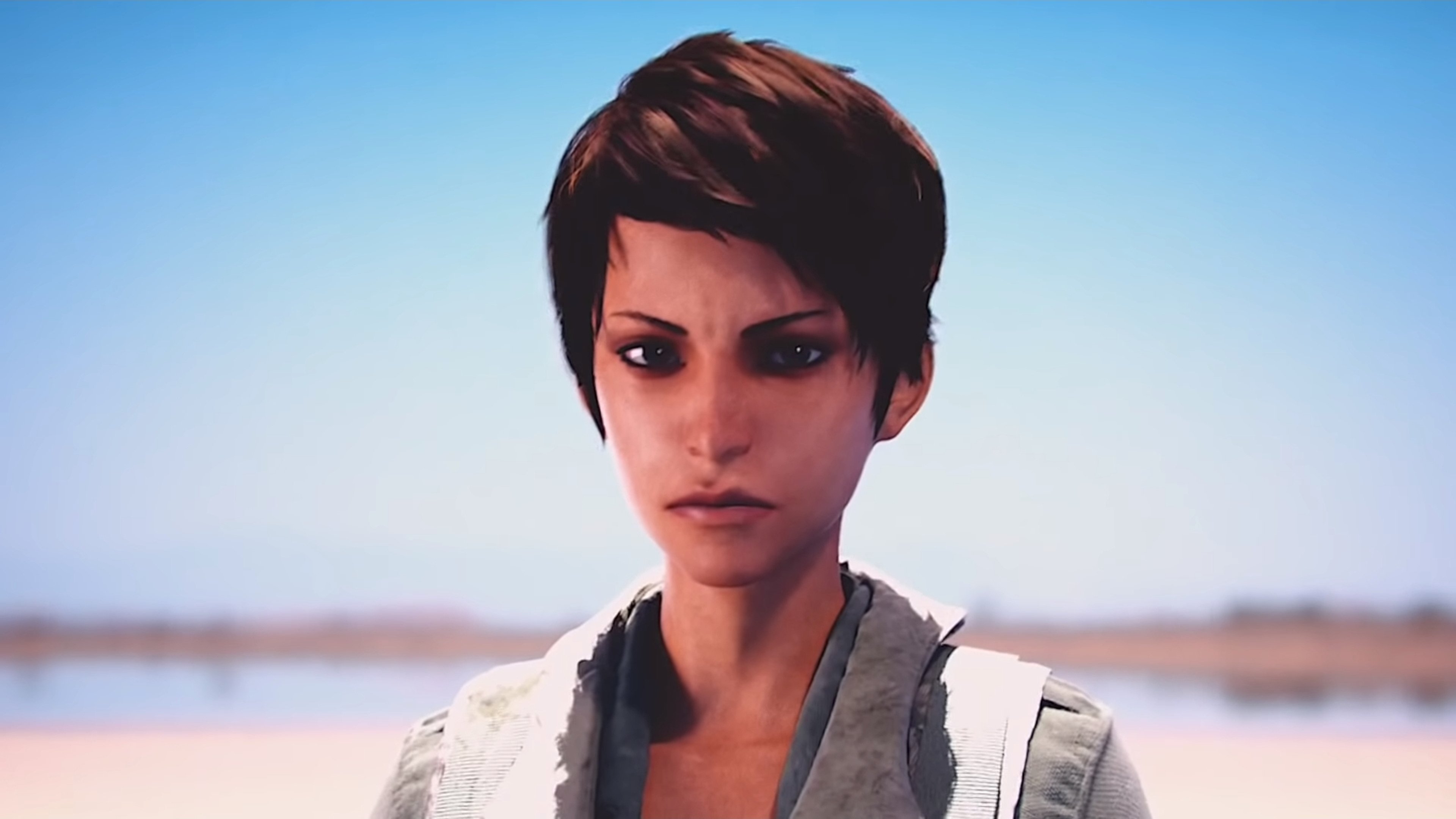 A young woman with light brown skin, hazel eyes, and brown hair, wearing practical work clothes.