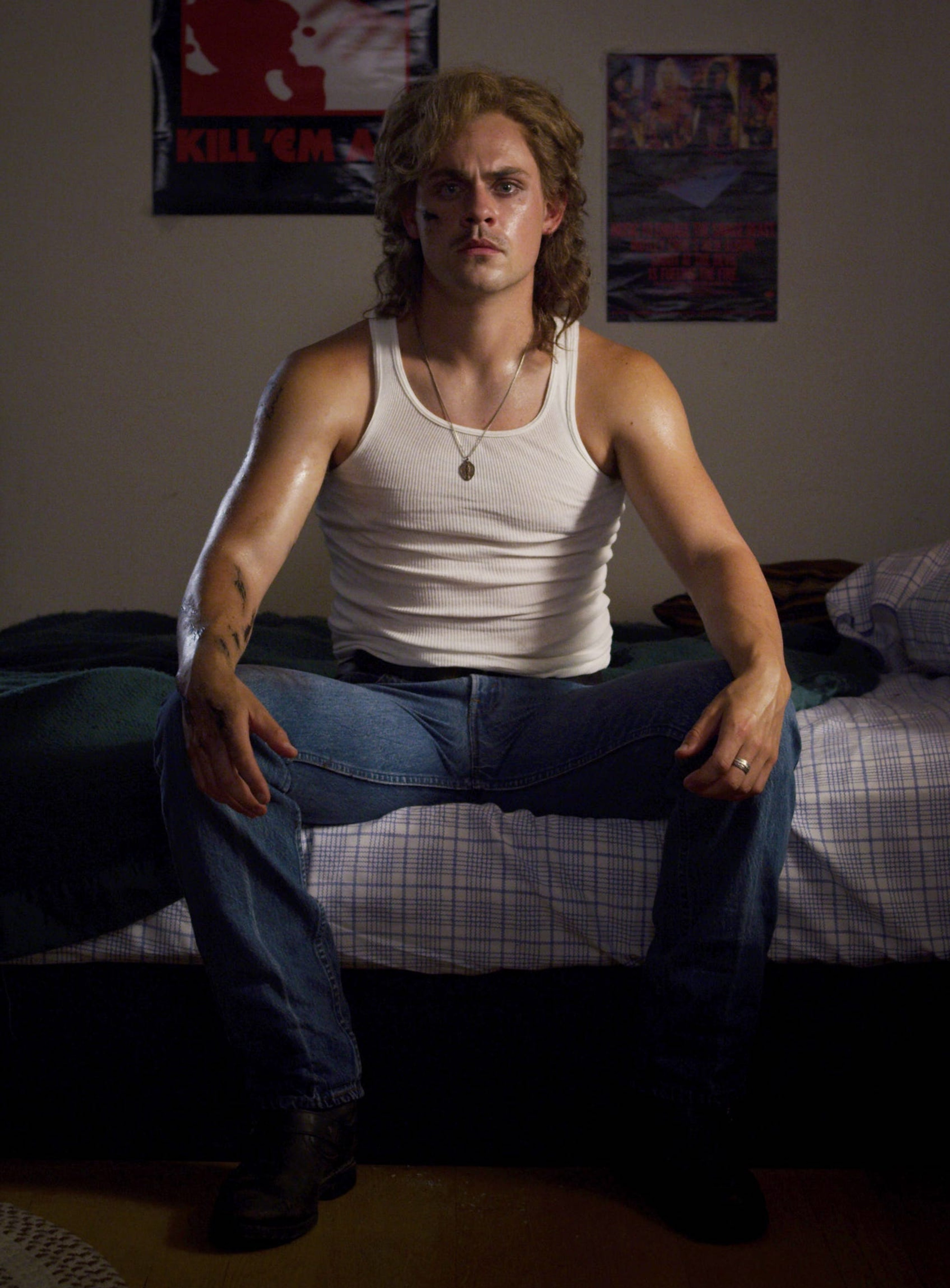 A young man with curly blonde hair sitting on a bed