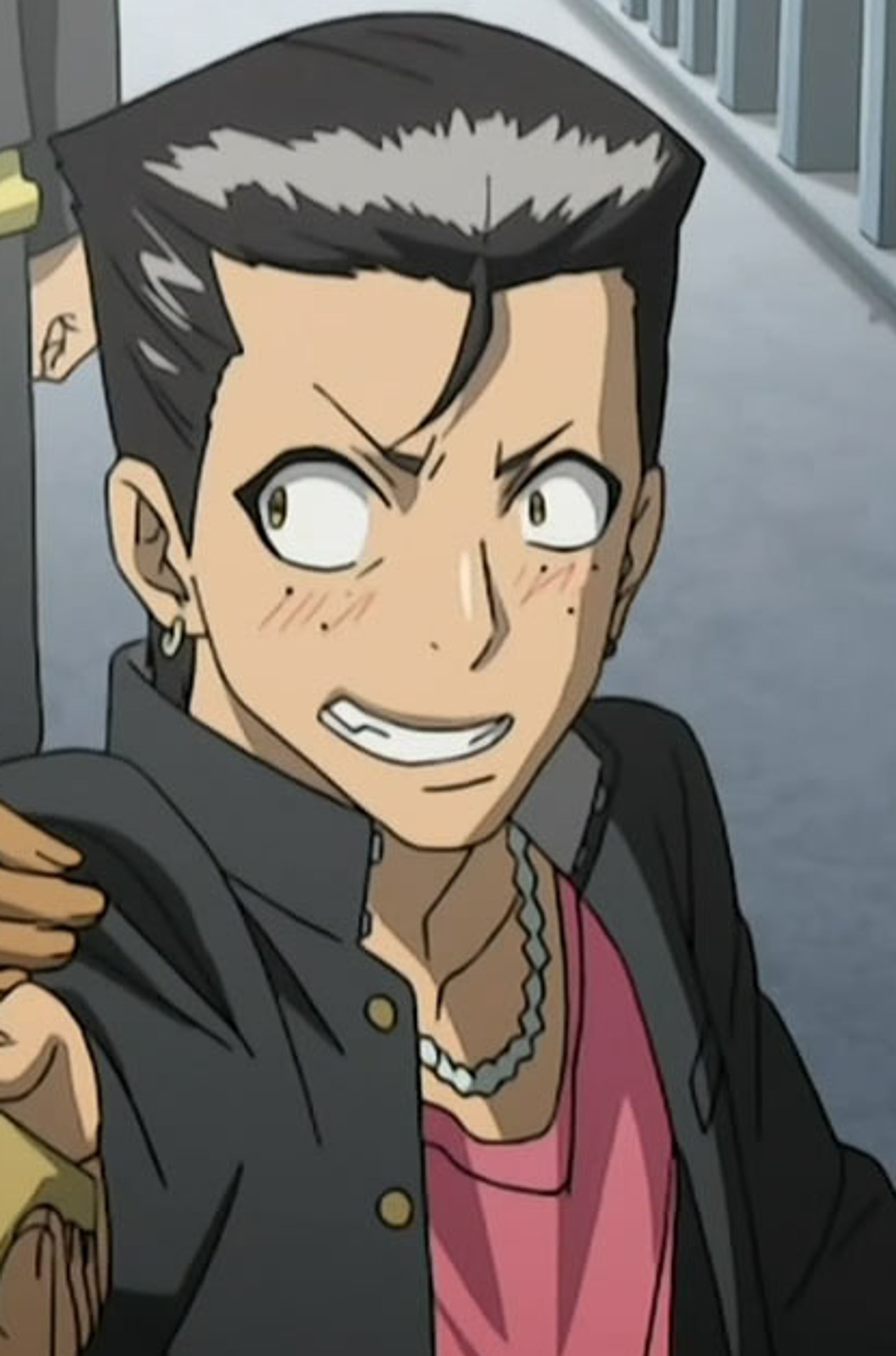 A young man with grayish-black hair, brown eyes, and freckles under his eyes, wearing a necklace and earrings, with a brash, defiant expression on his face.