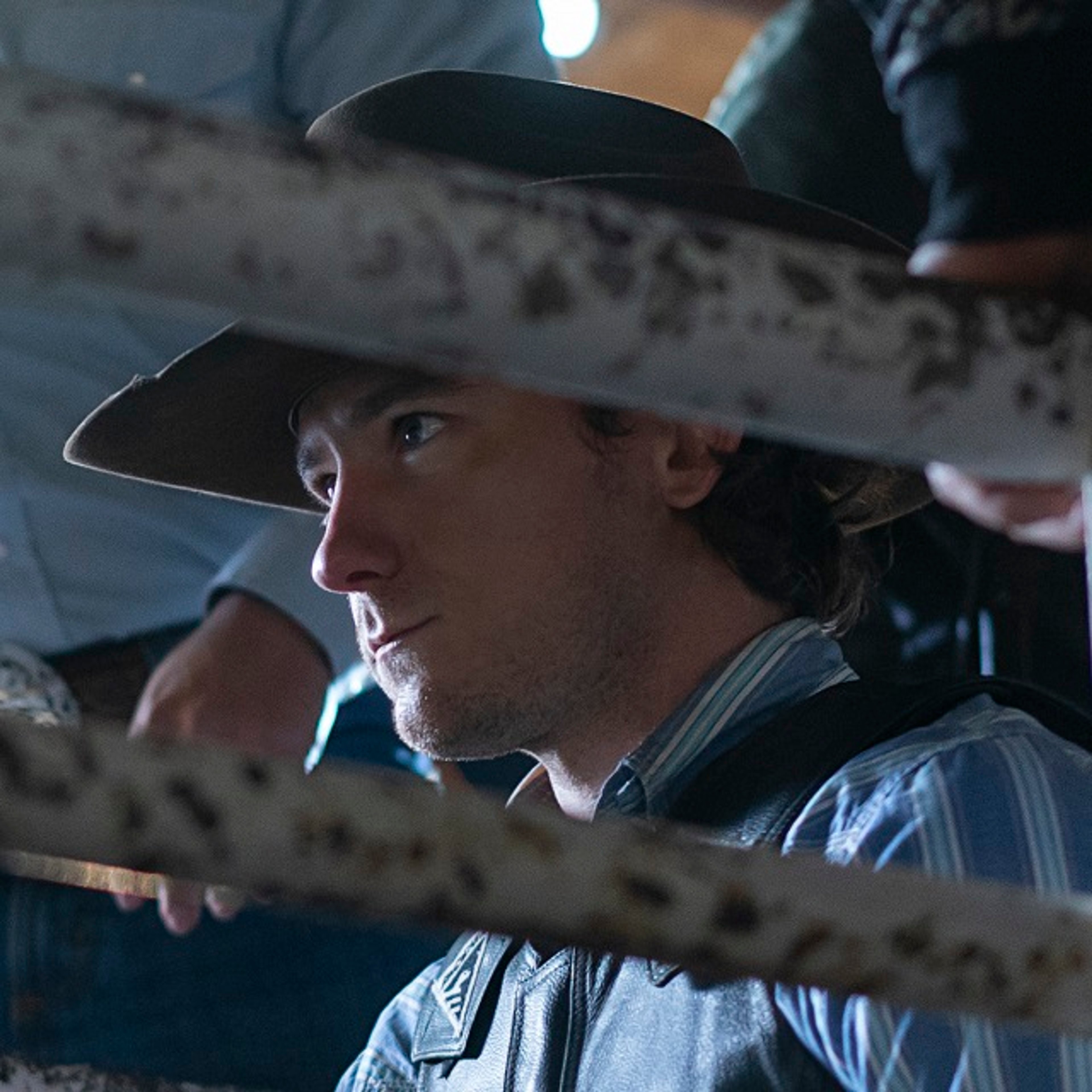 A young man in a cowboy hat and plaid shirt with a serious expression