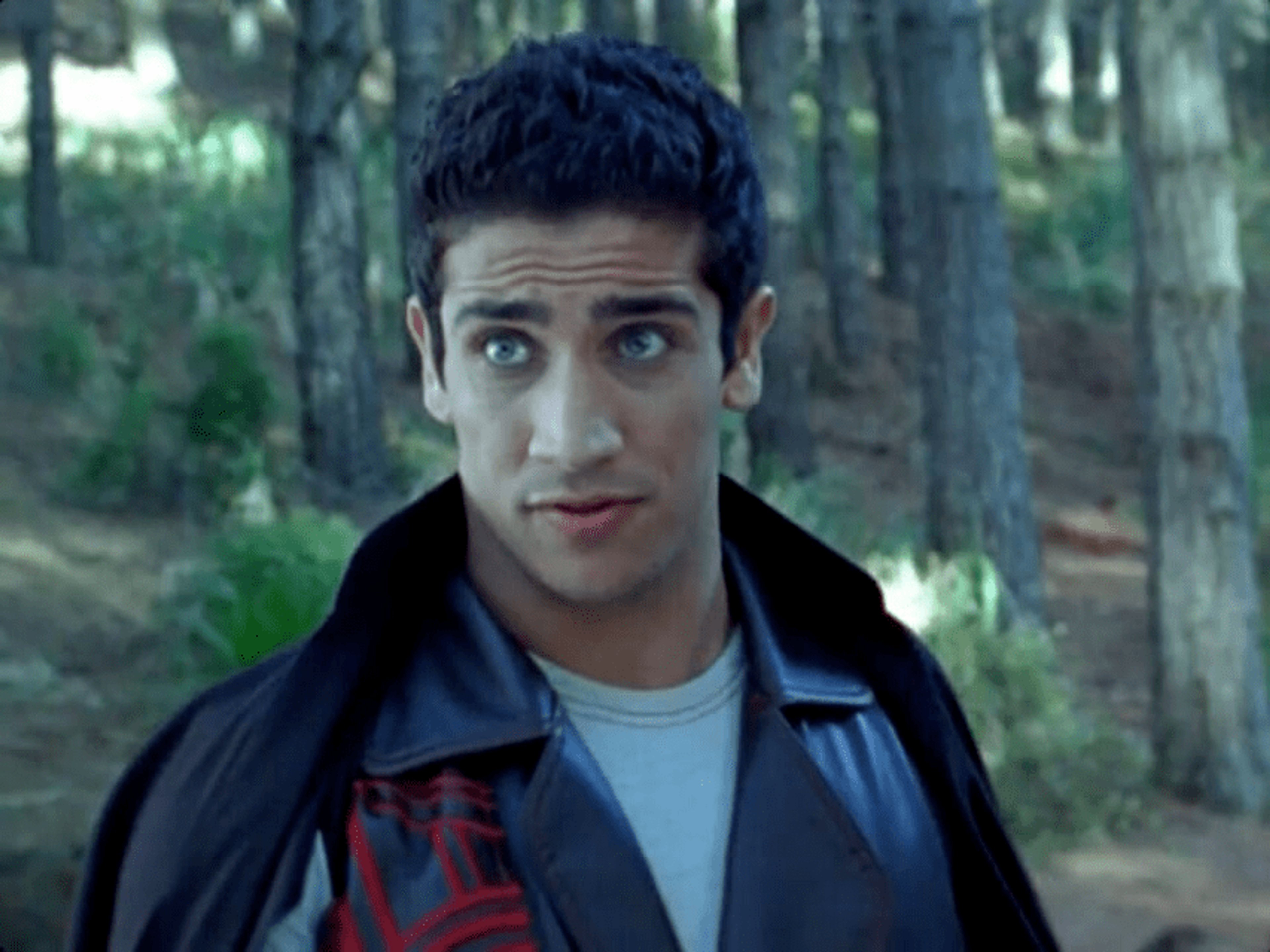 A young man with dark hair wearing a red jacket in a forest setting