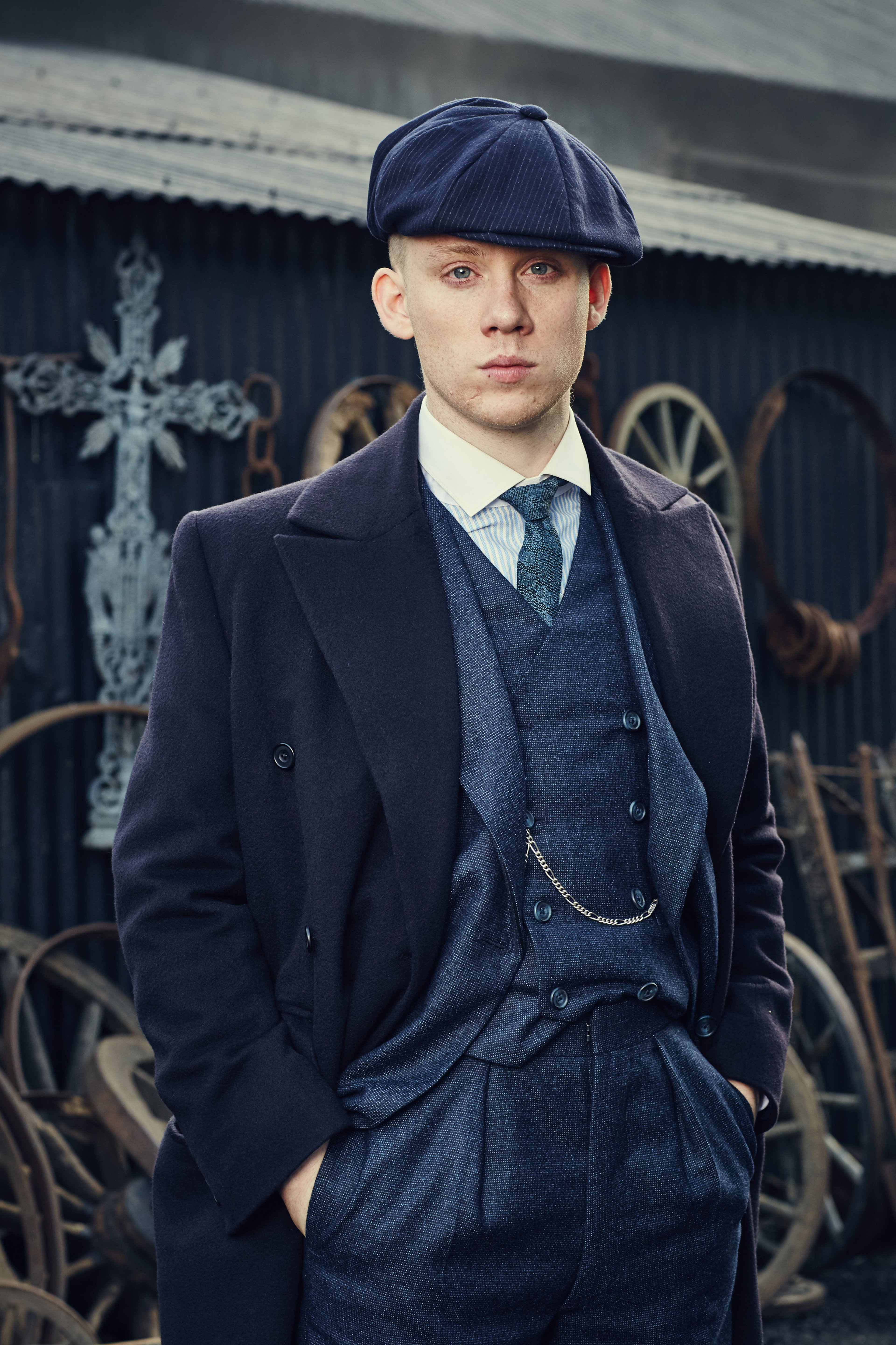 A man in a dark suit and flat cap standing in front of an ornate building