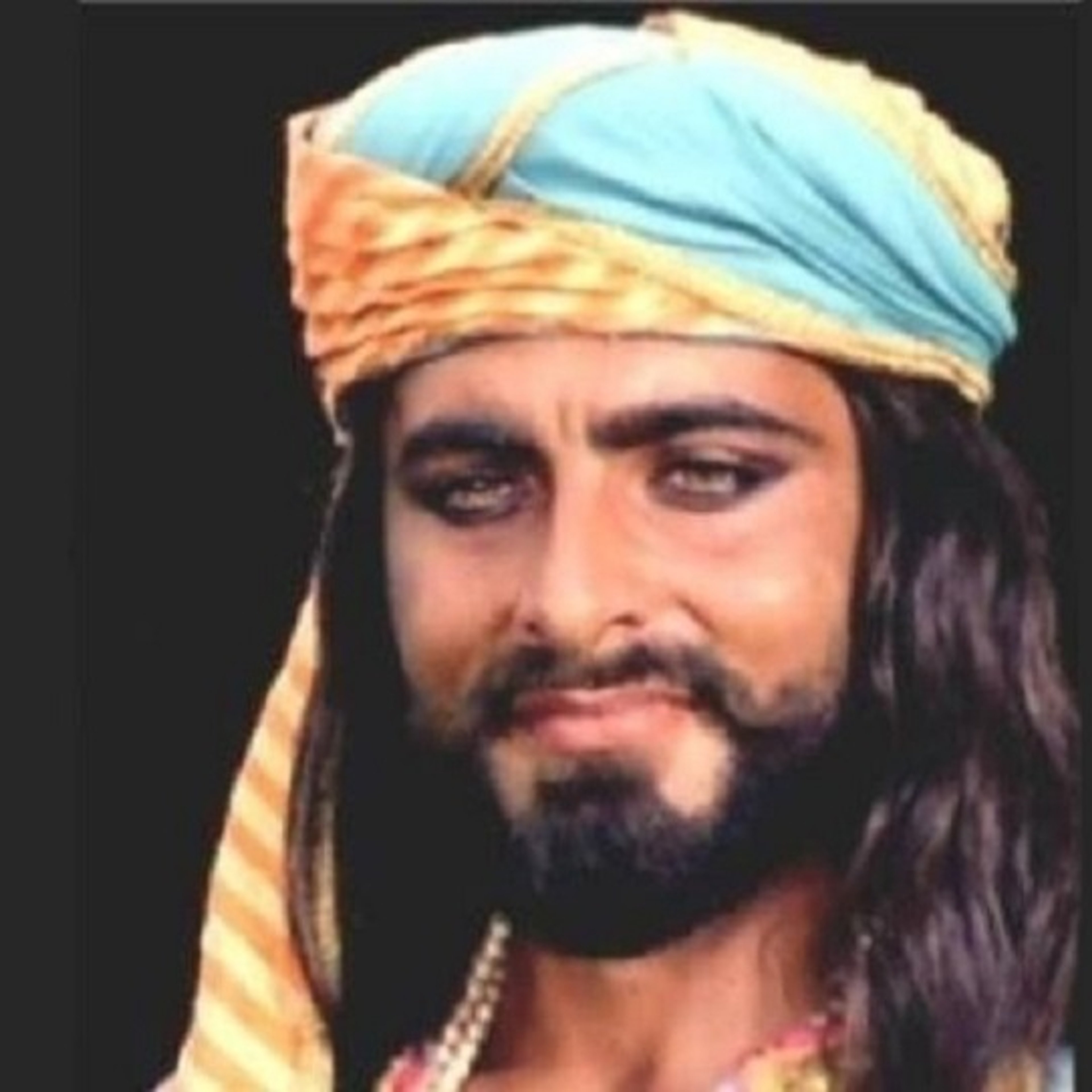 A man with a dark beard and mustache wearing a turban and ornate clothing