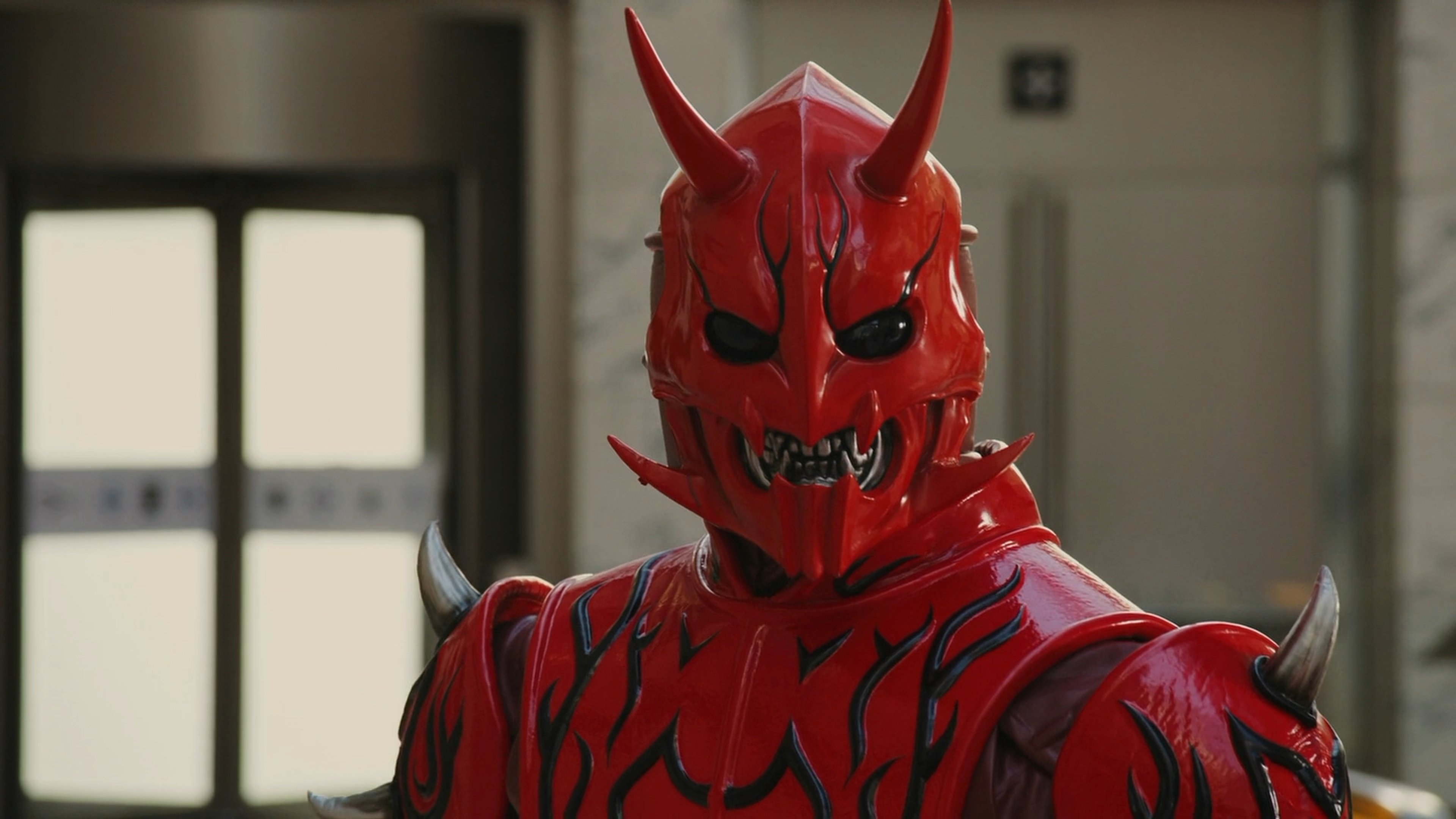 A red, oni-like creature with horns and a peach motif, wearing a red bodysuit with armor-like elements.