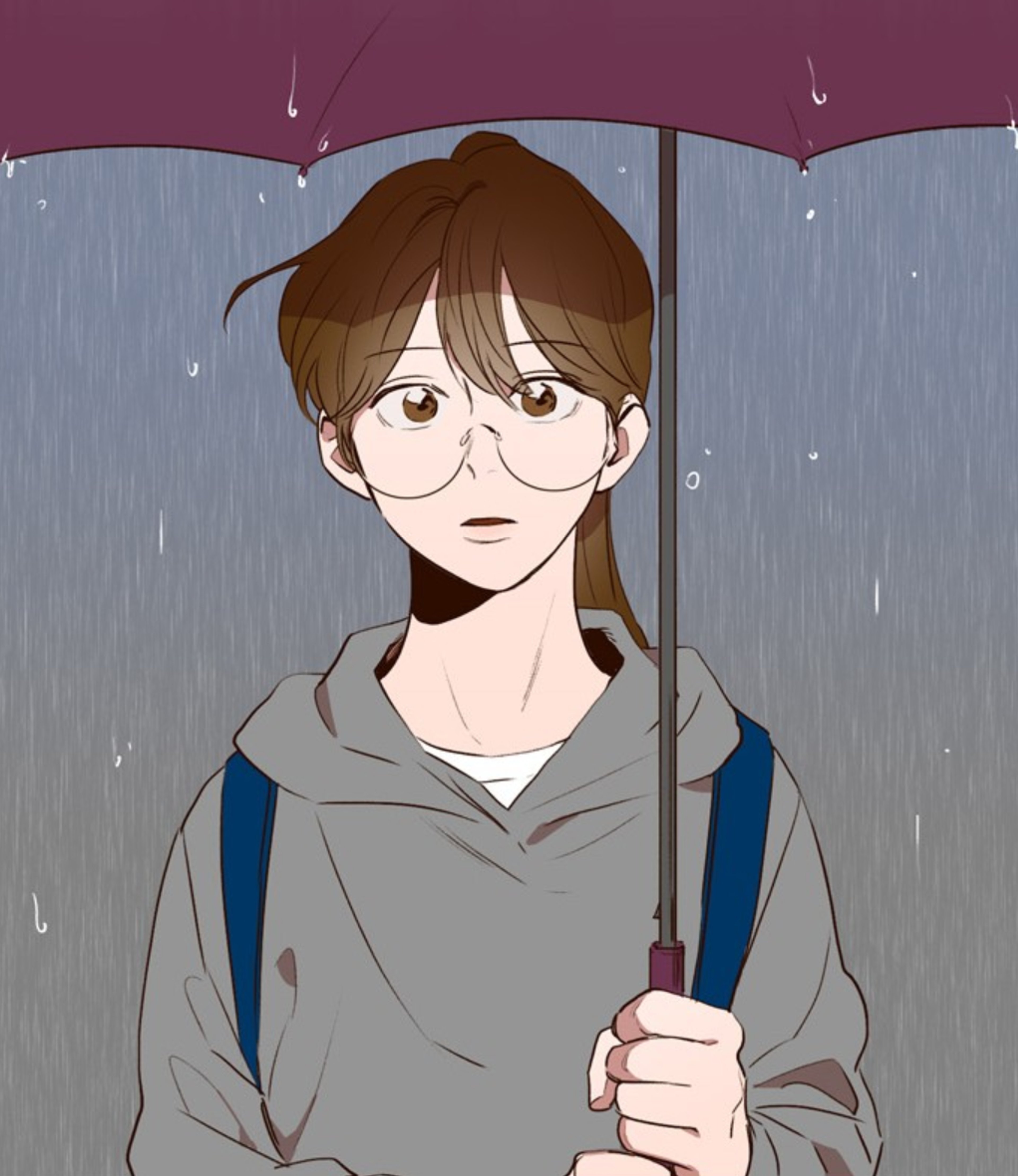 A young woman with short dark hair wearing glasses and a gray hooded jacket, standing in the rain and holding an umbrella.
