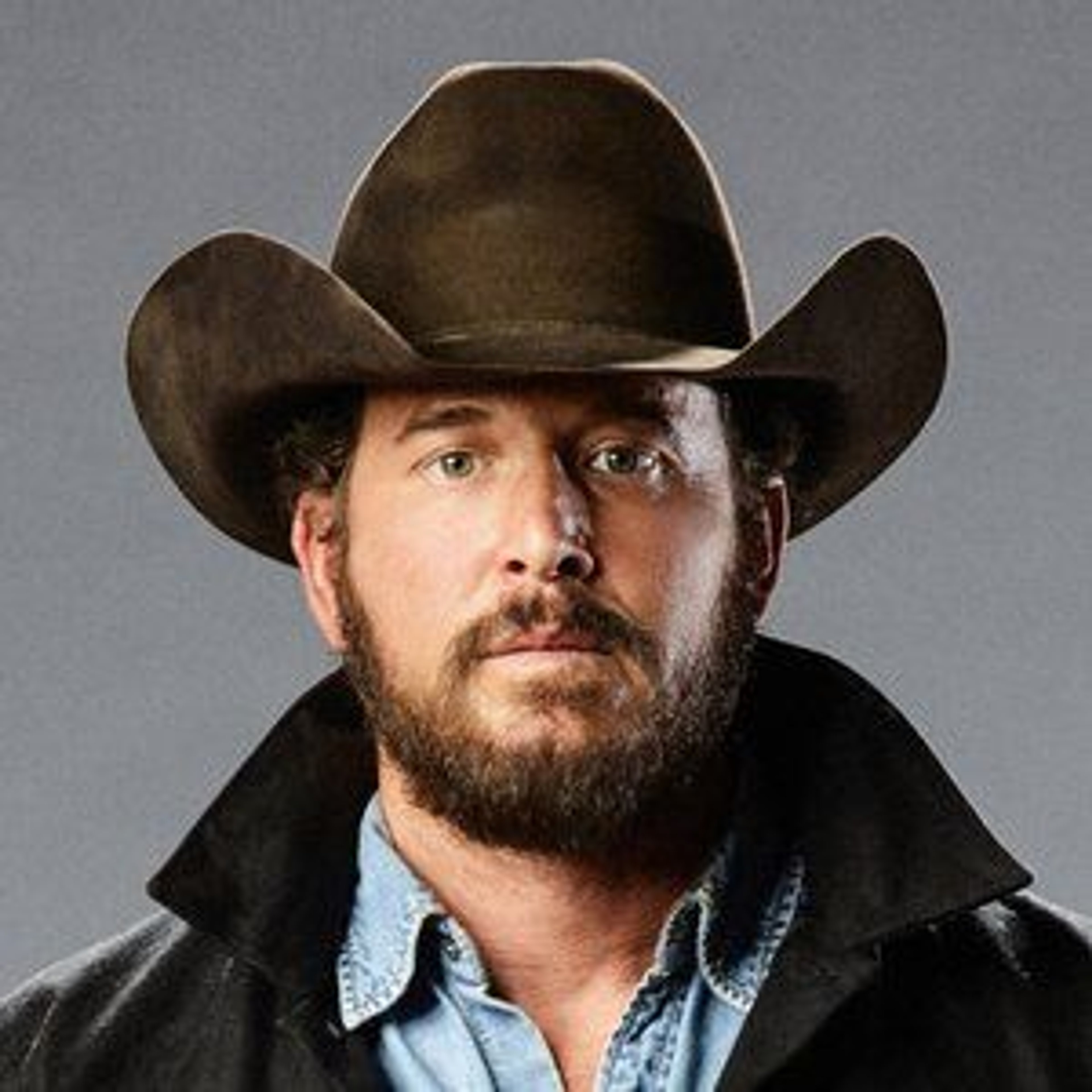 A middle-aged man with a rugged appearance wearing a black cowboy hat and denim jacket