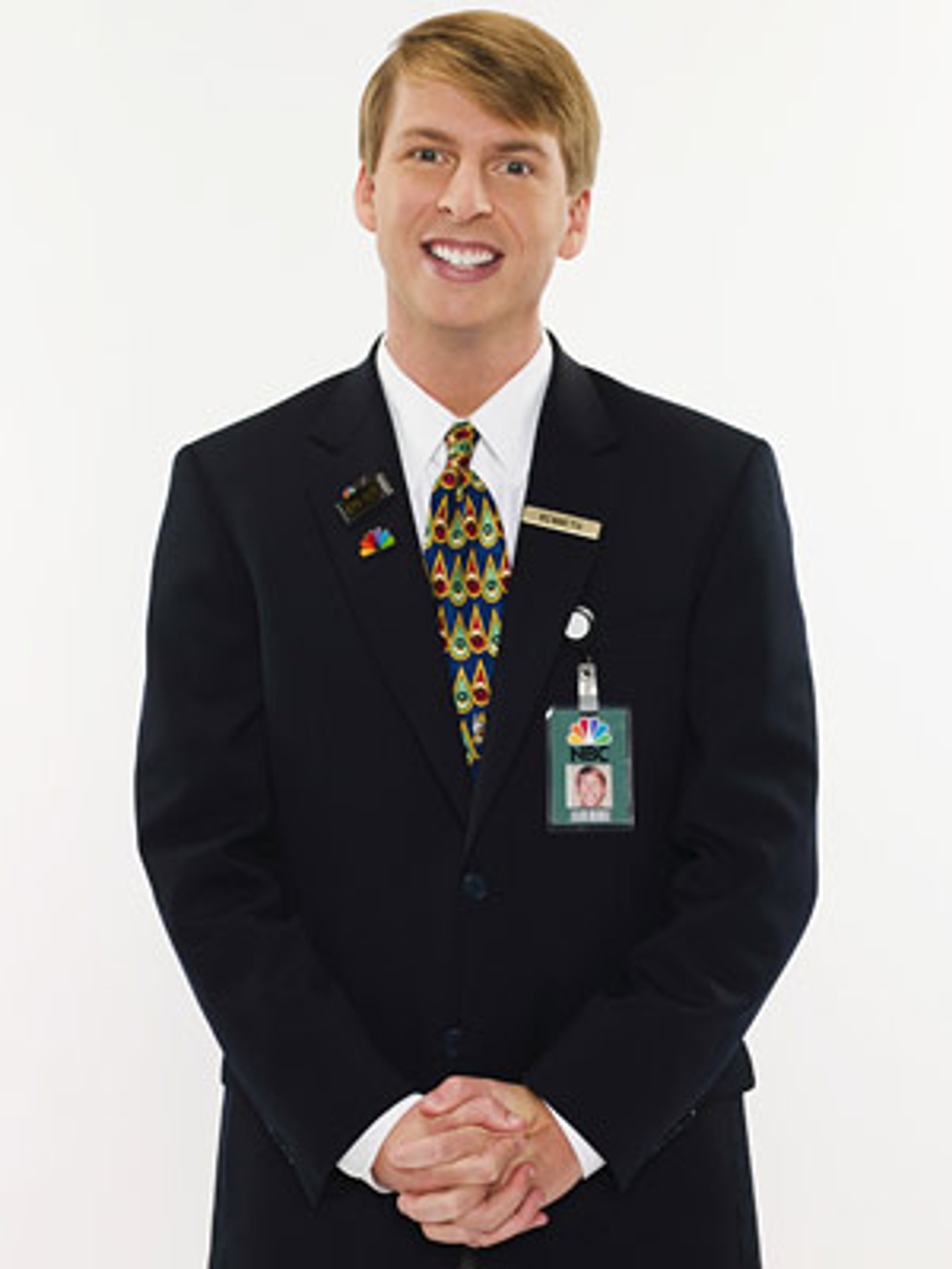 A man in a black suit and colorful tie smiling at the camera