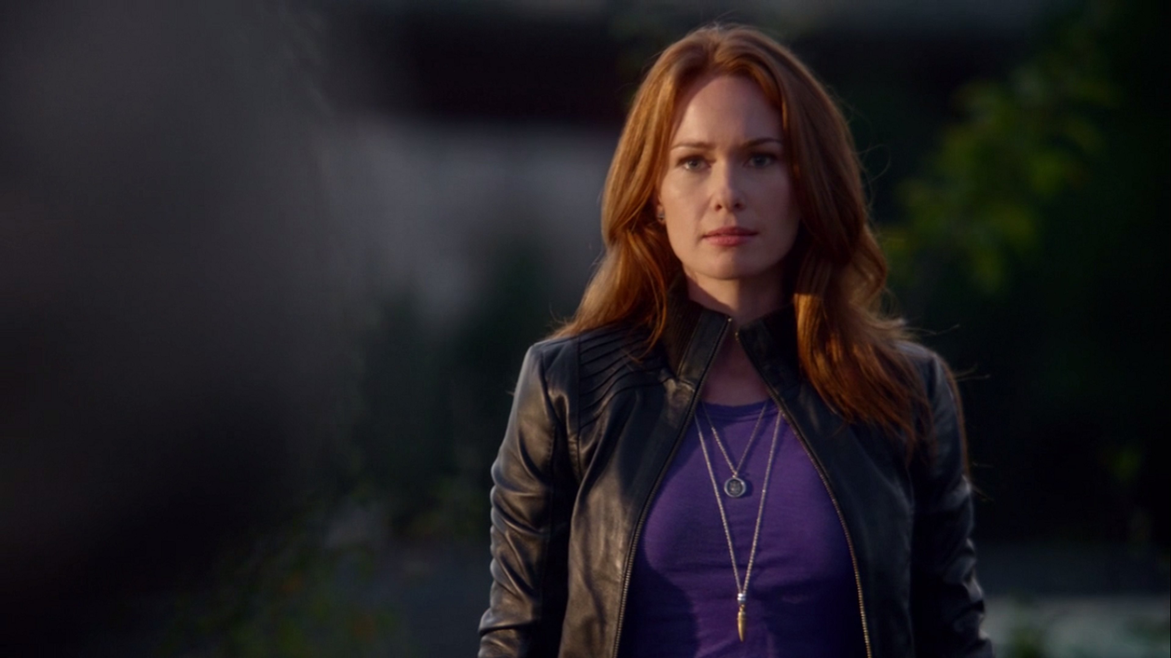 A woman with red hair wearing a purple shirt and black leather jacket standing outdoors at night.