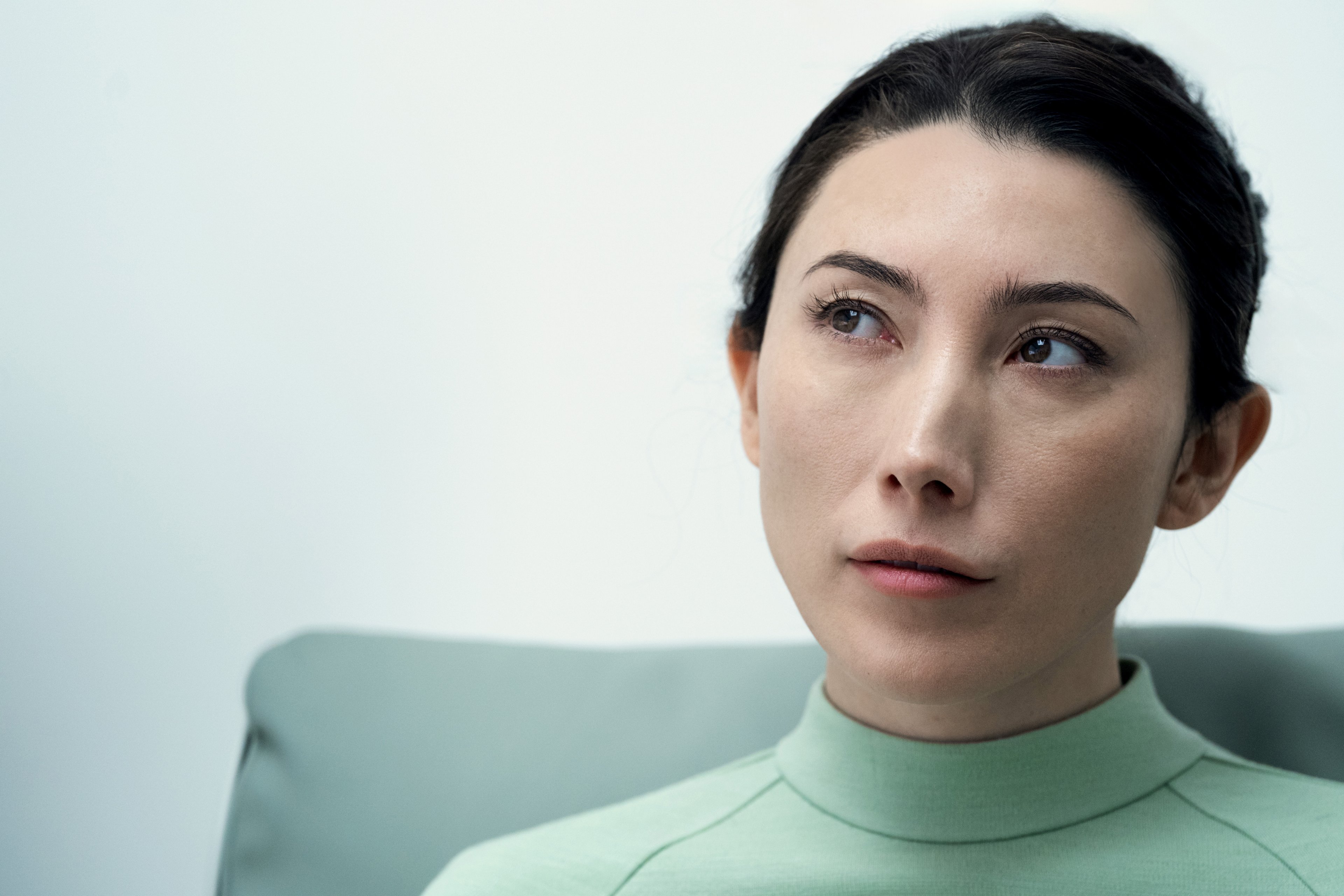 A woman with dark hair wearing a light green turtleneck sweater in a professional setting