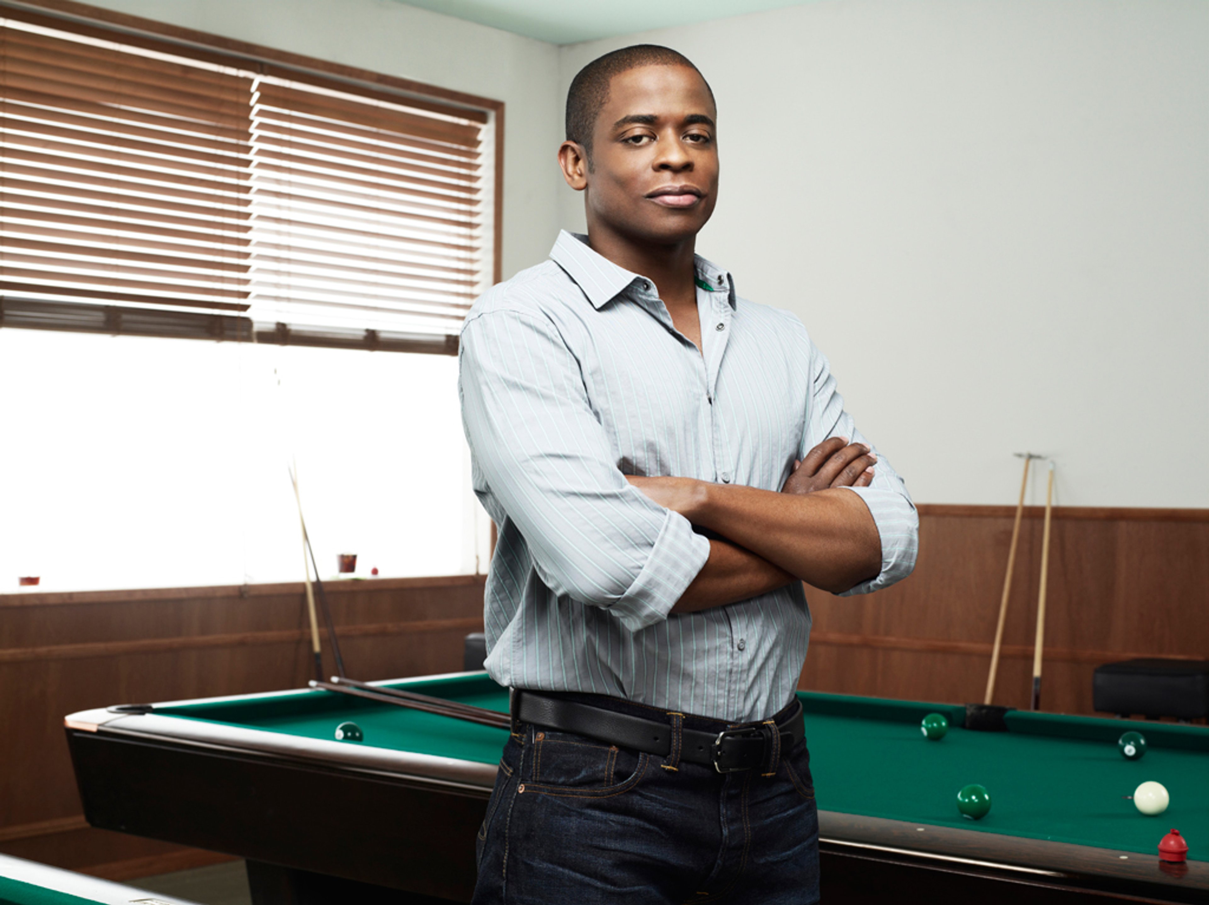 A middle-aged Black man with a serious expression, wearing a light blue shirt and standing in an indoor setting.