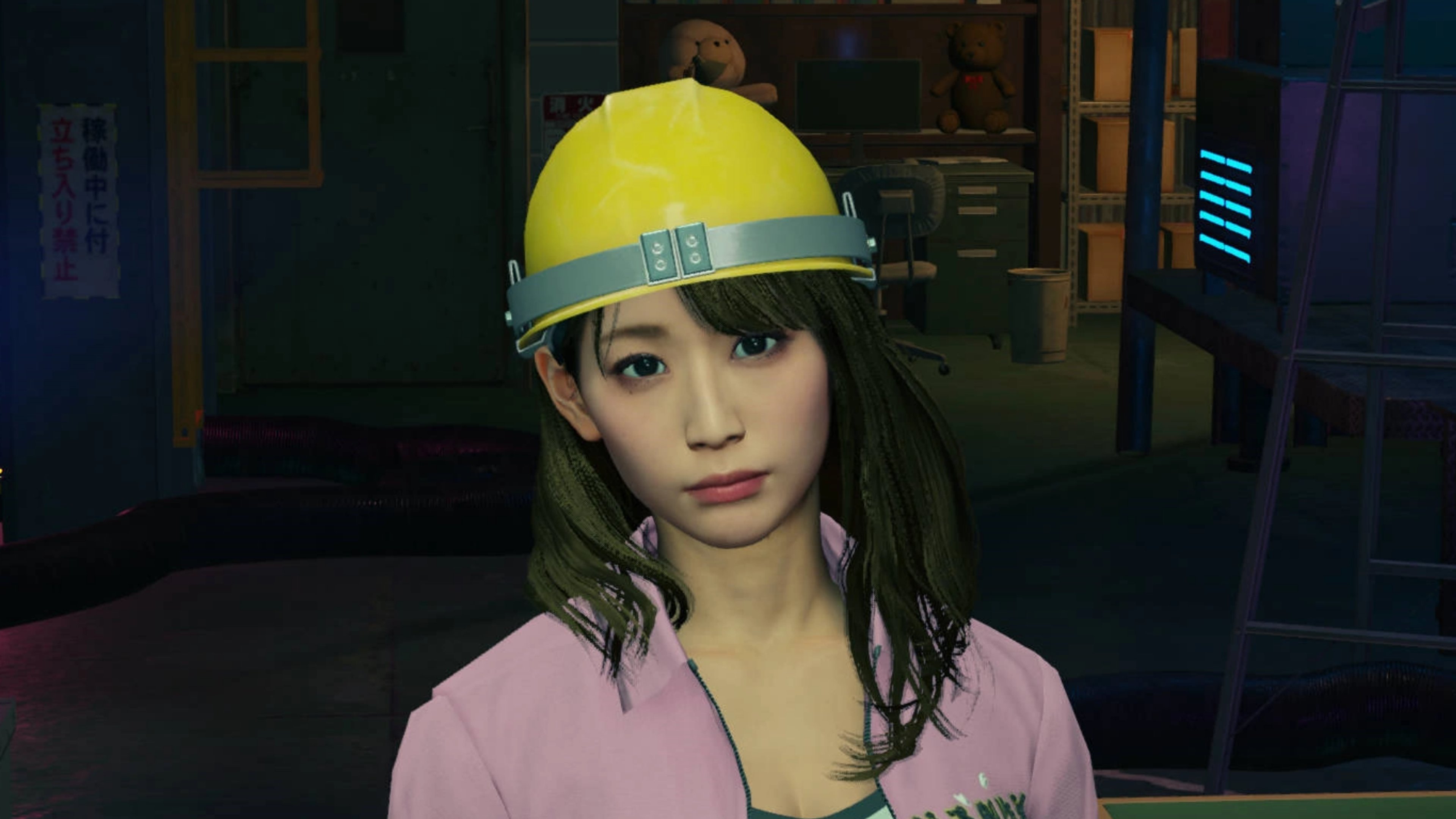 A young woman with long dark hair wearing a pink shirt and yellow hard hat, standing in an industrial setting.