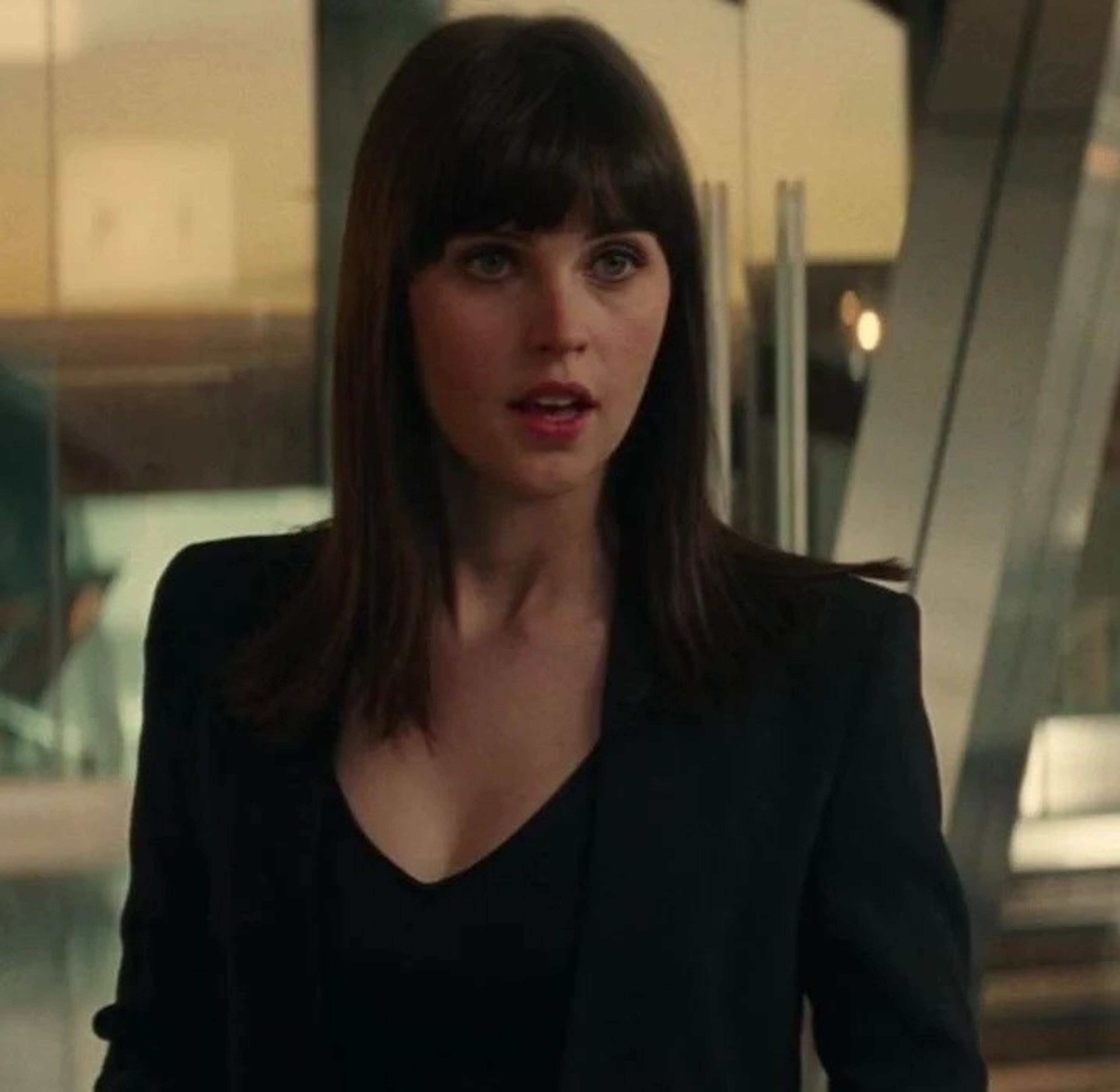 A woman in a black suit jacket with a serious expression