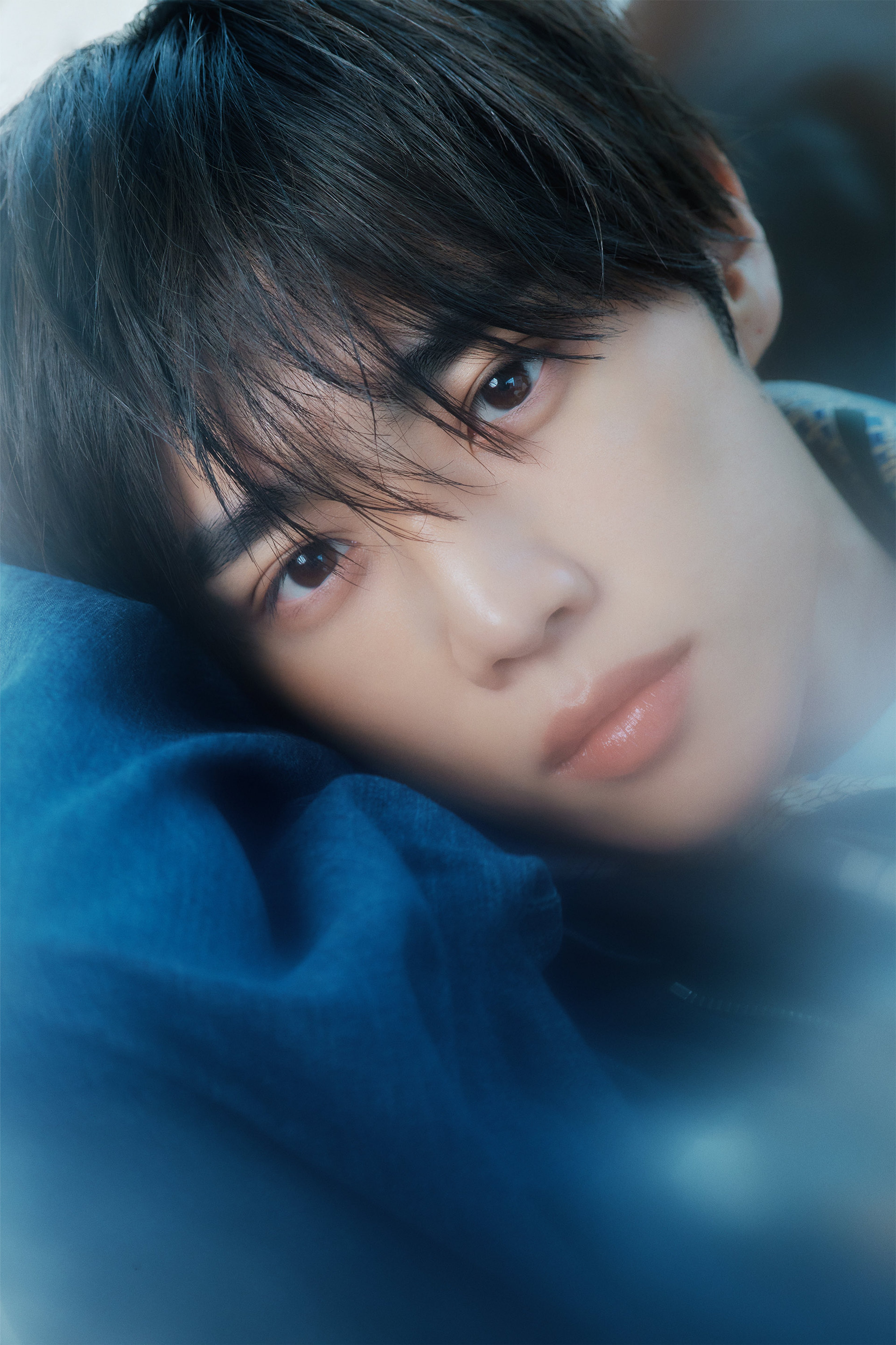 A young man with dark hair wearing a blue sweater or jacket, looking directly at the camera.