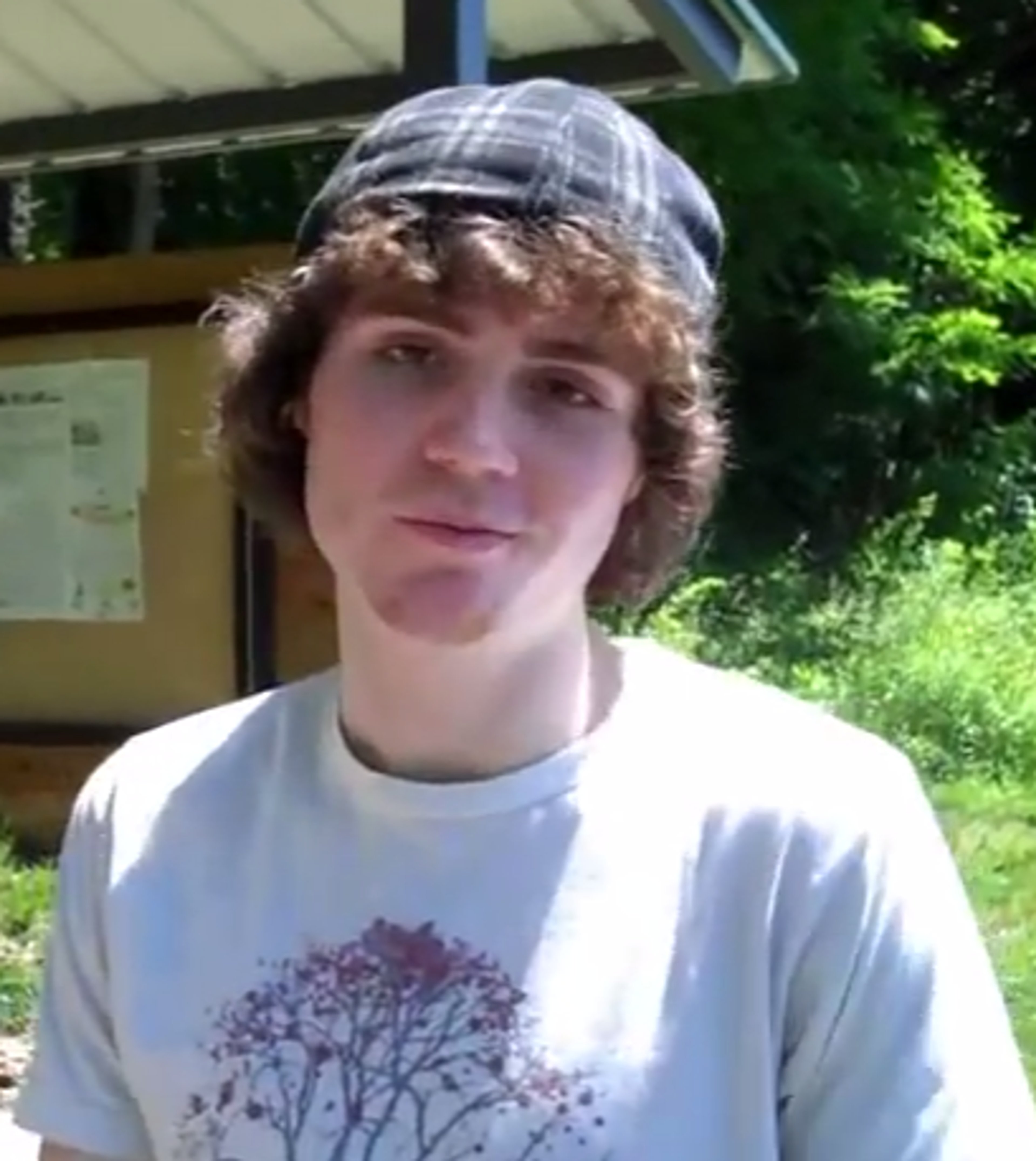 A young man with curly brown hair wearing a white t-shirt