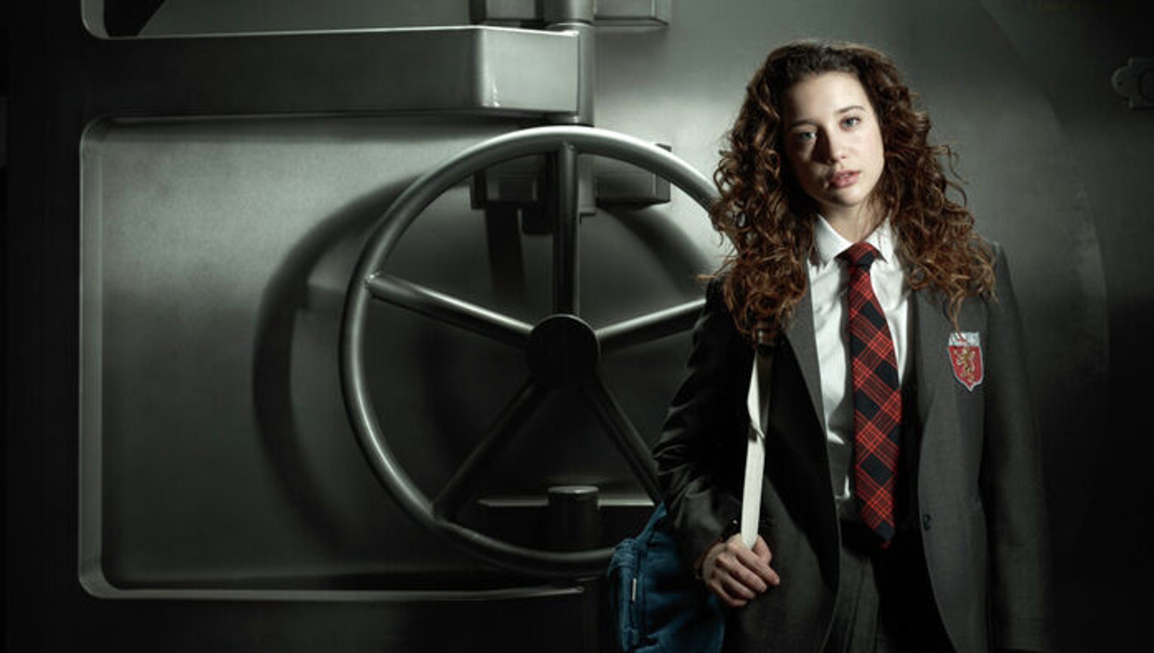 A young woman in a school uniform standing in front of a large metal vault door