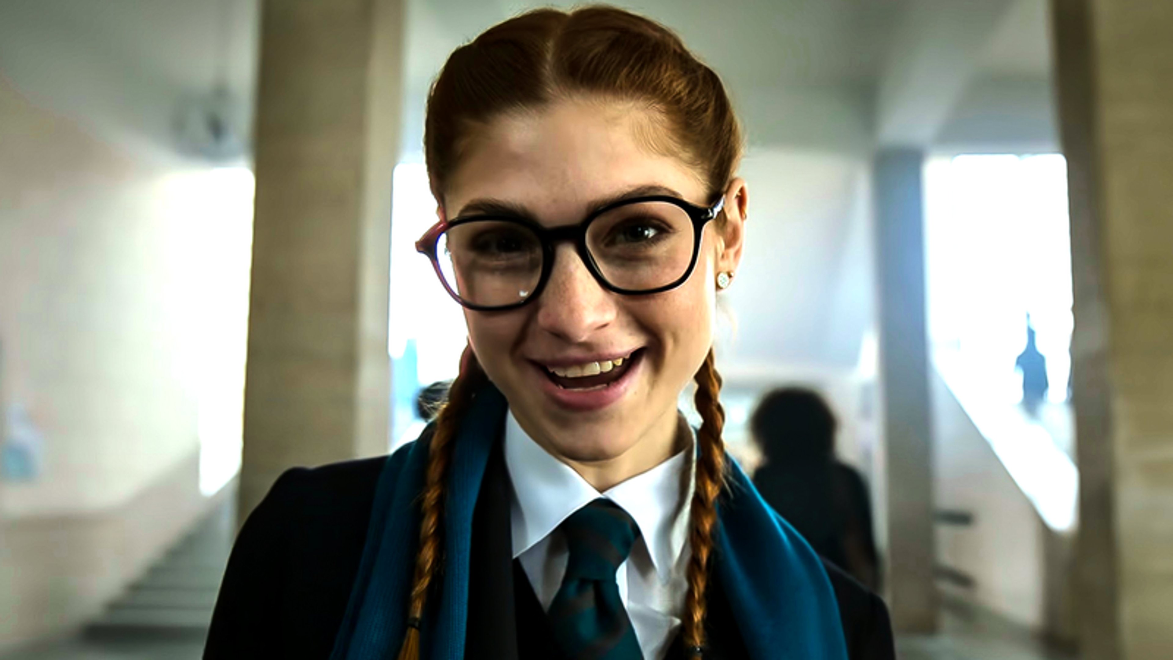 A young woman with braided hair and glasses, wearing a school uniform and smiling