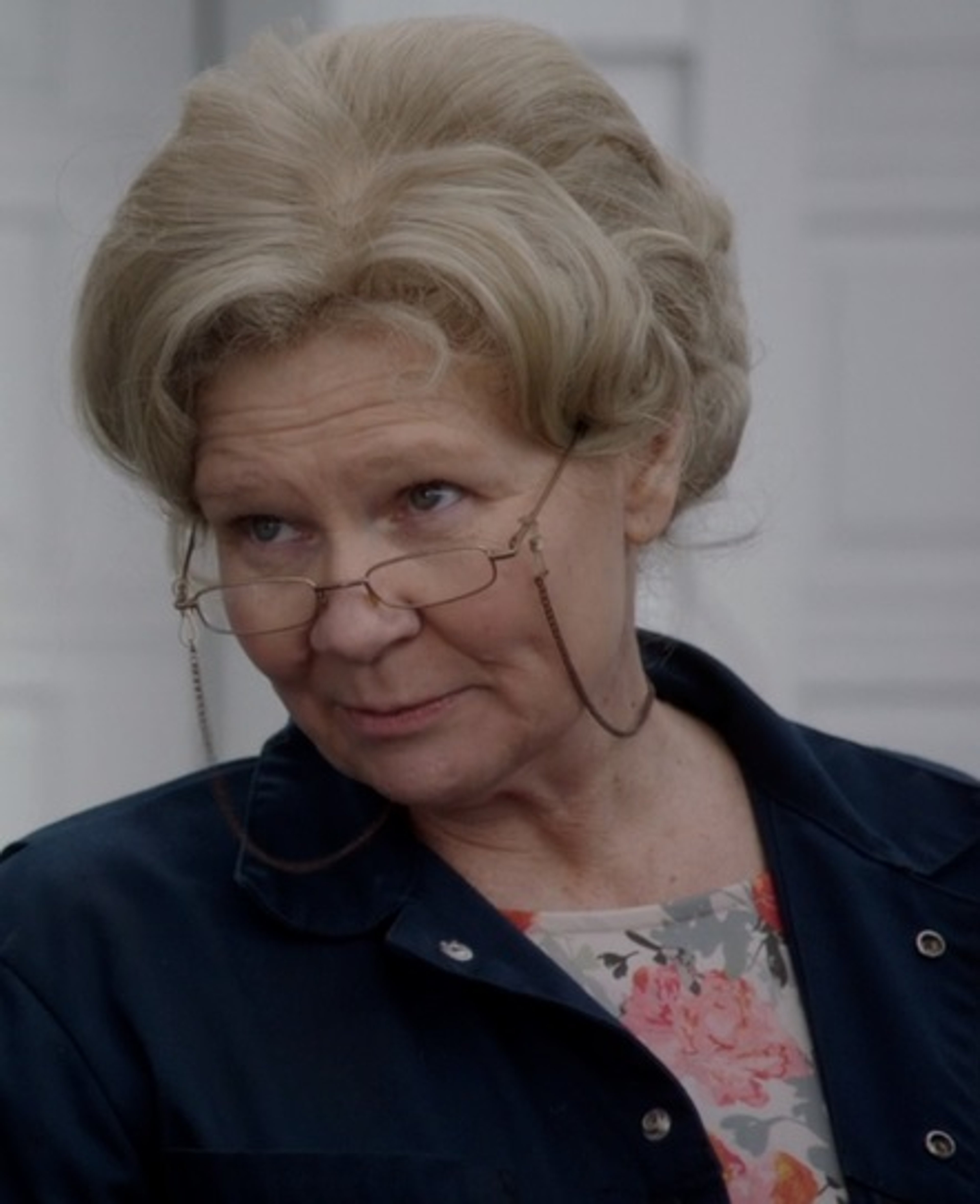 An elderly woman with short gray hair and glasses wearing a dark jacket