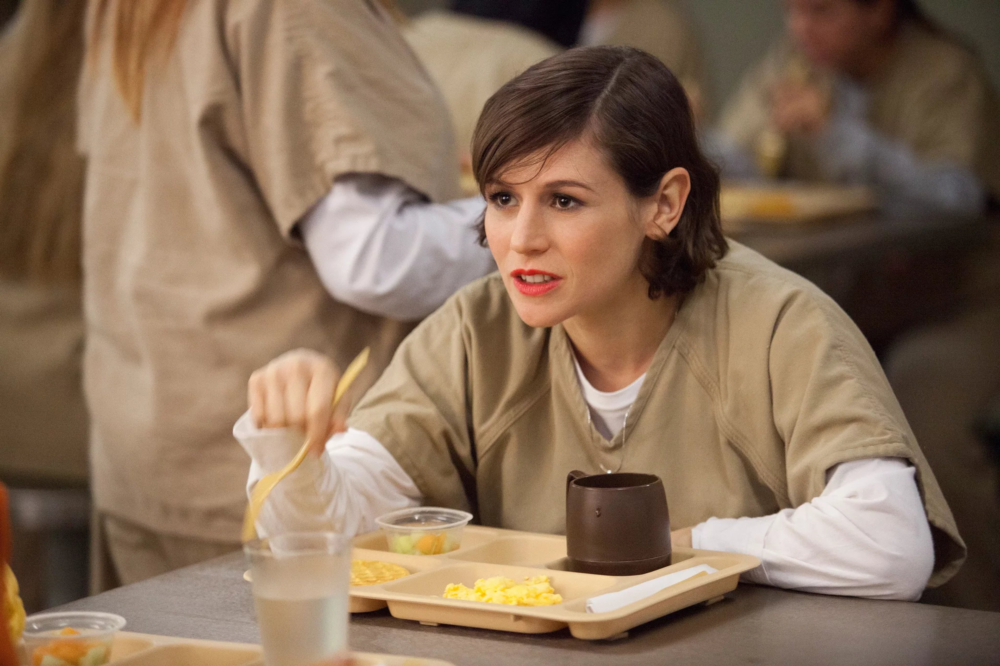 A young woman with dark hair sitting at a table in a cafeteria or dining hall.