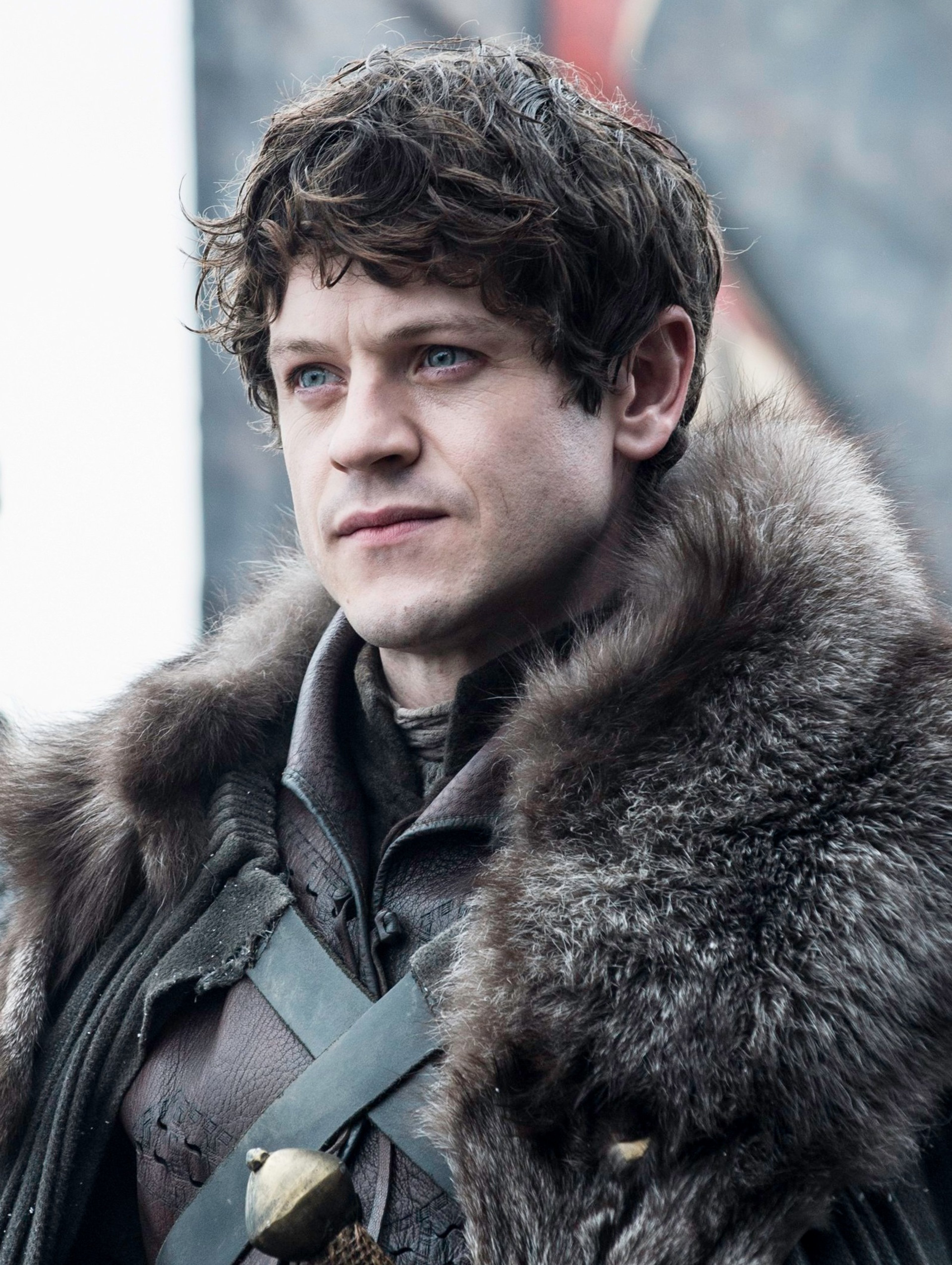 A man with dark, curly hair wearing a fur-trimmed coat