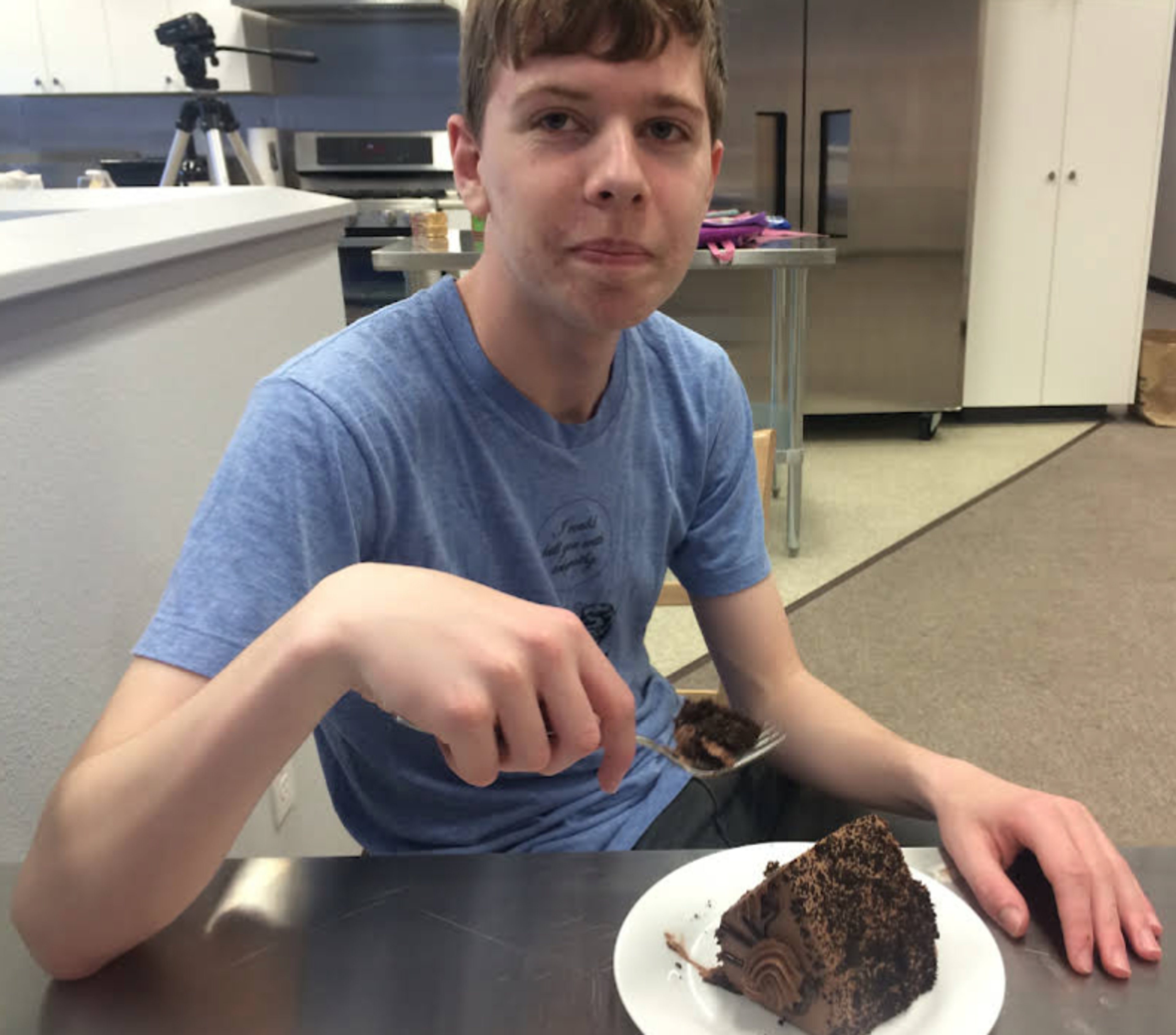 A young man sitting at a table holding a plate with a dessert item on it.