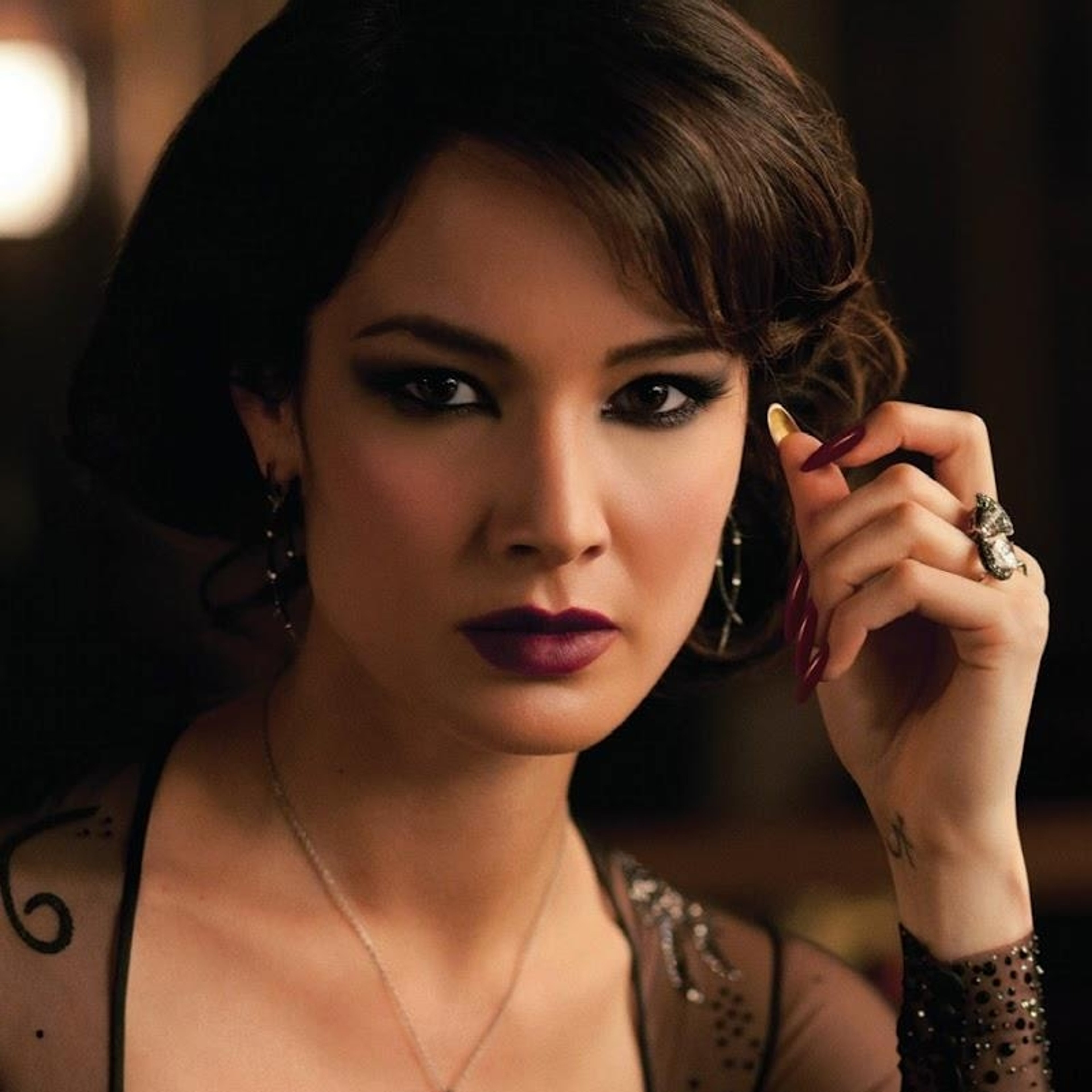 A woman with dark hair and dramatic makeup looking intensely at the camera