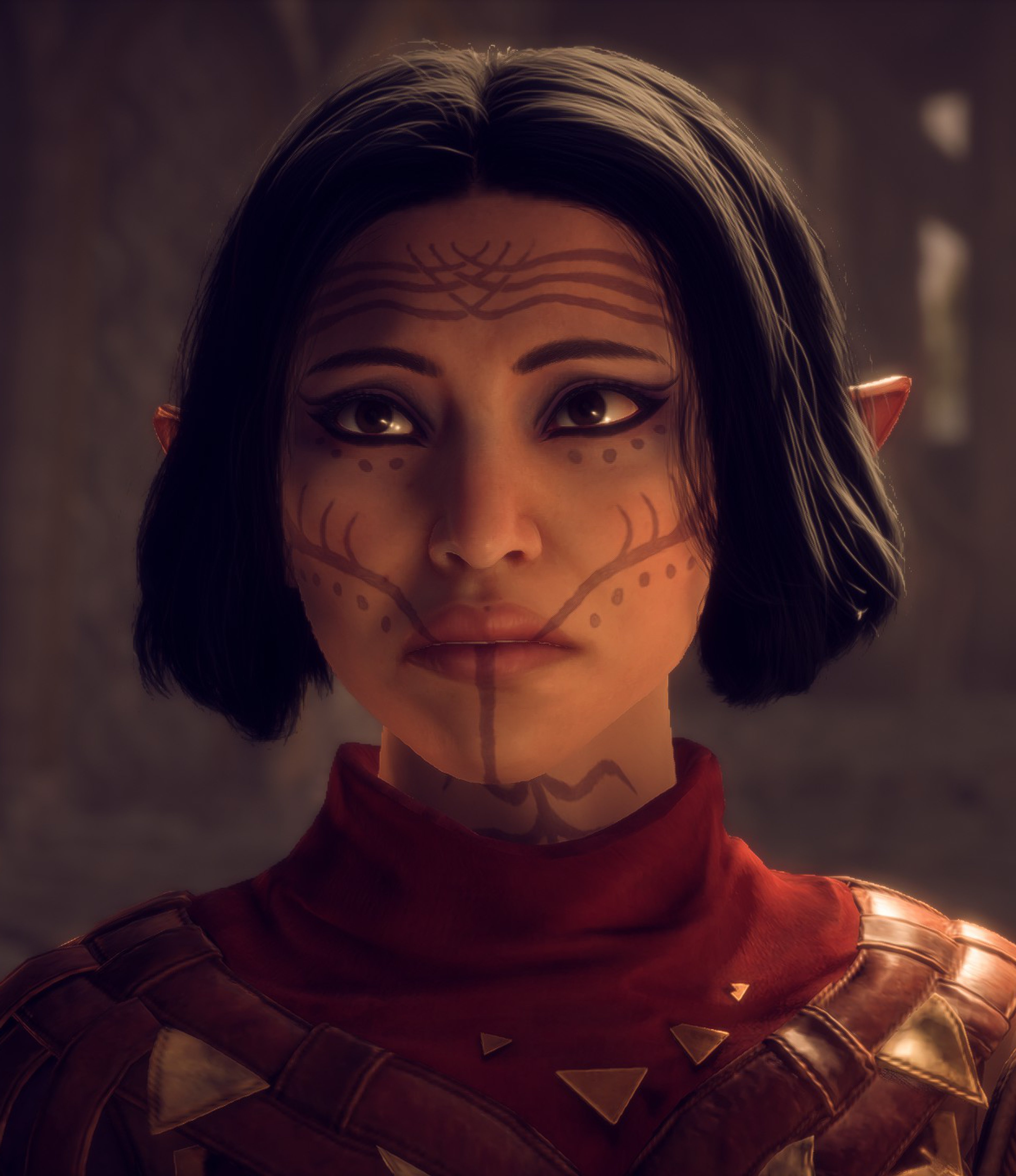 A female elf character with short dark hair, freckles, and facial tattoos wearing a red and gold armored outfit.