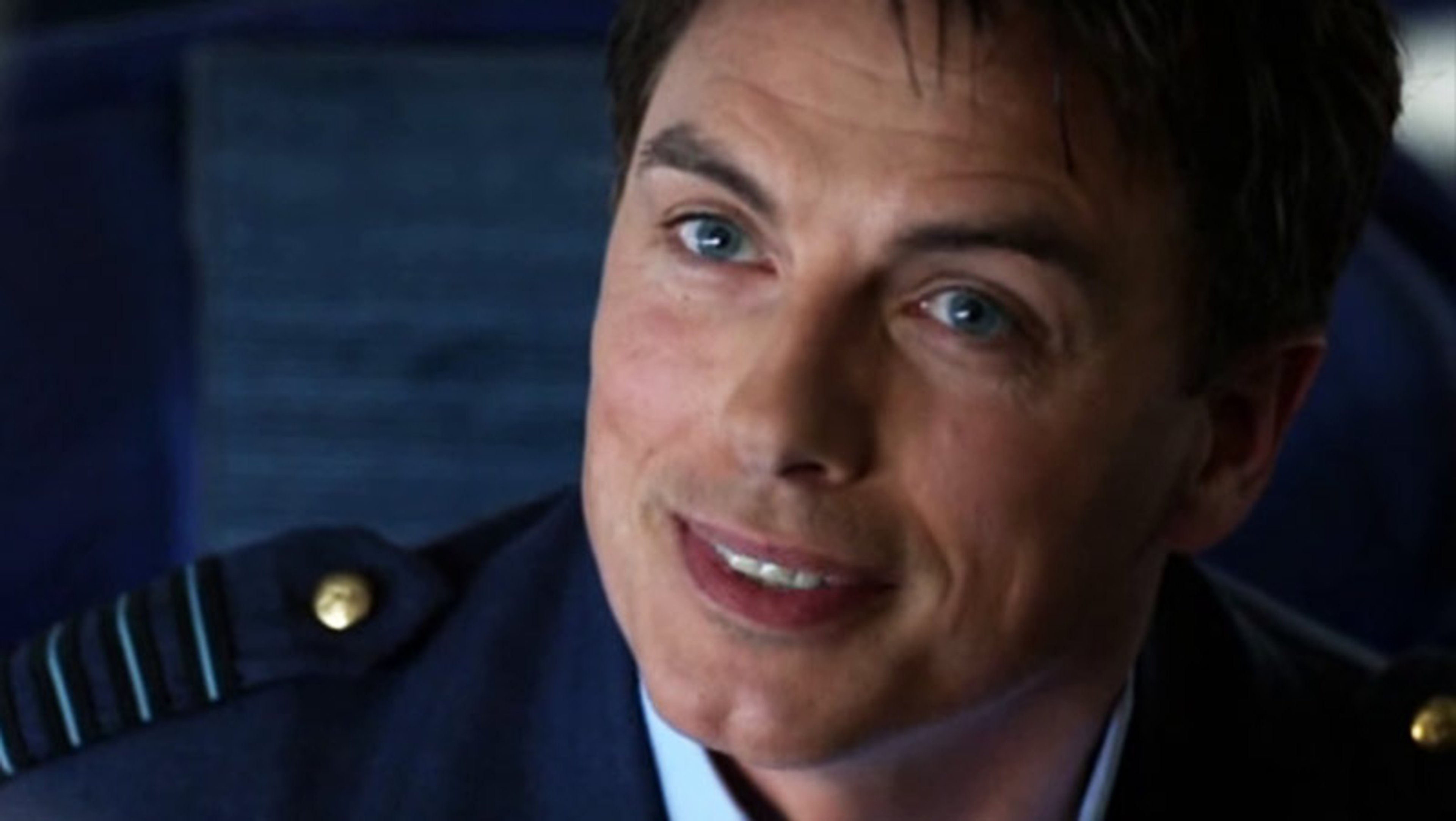 A close-up portrait of a smiling man in a military-style uniform