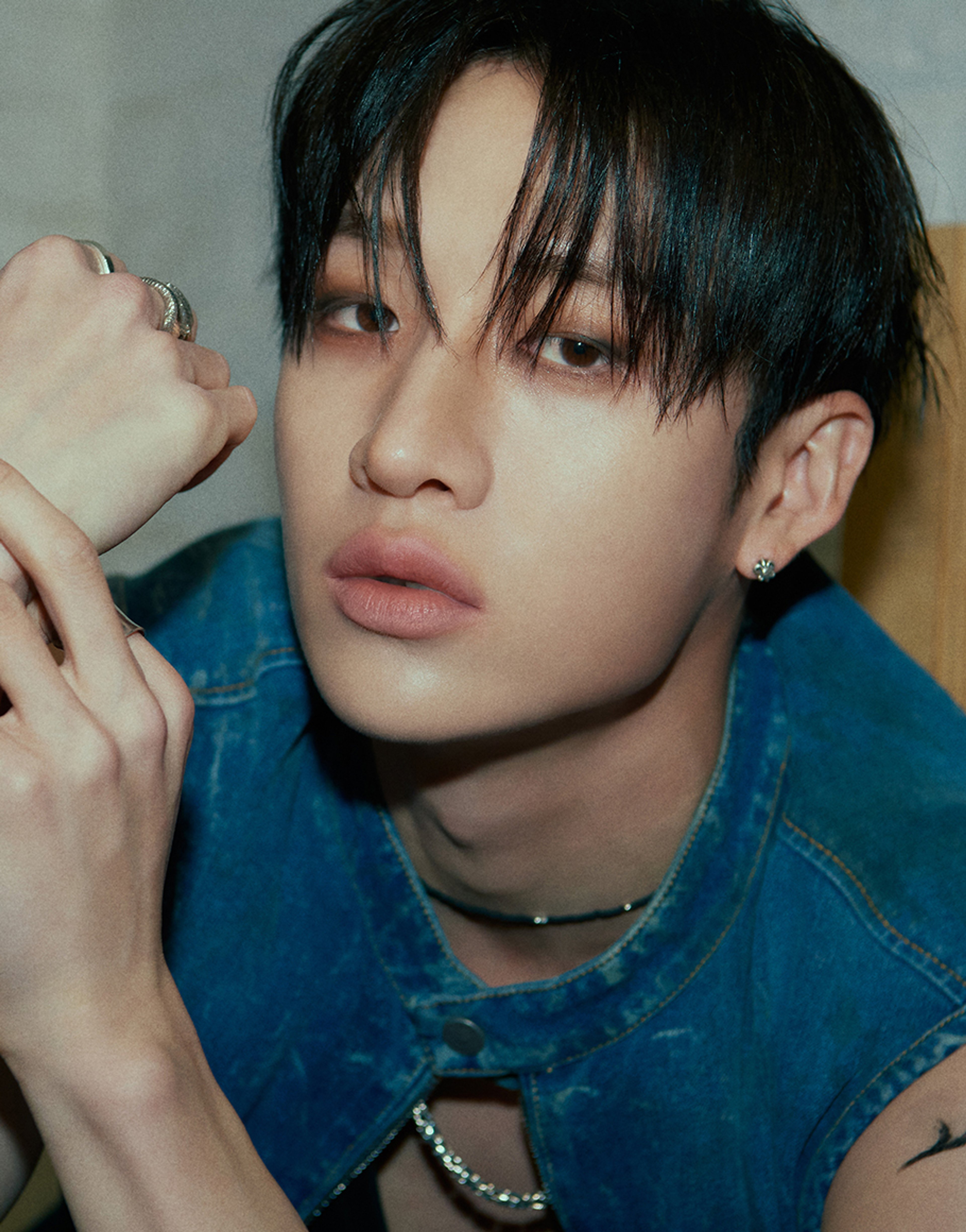 A young man with dark hair and a serious expression, wearing a denim jacket.