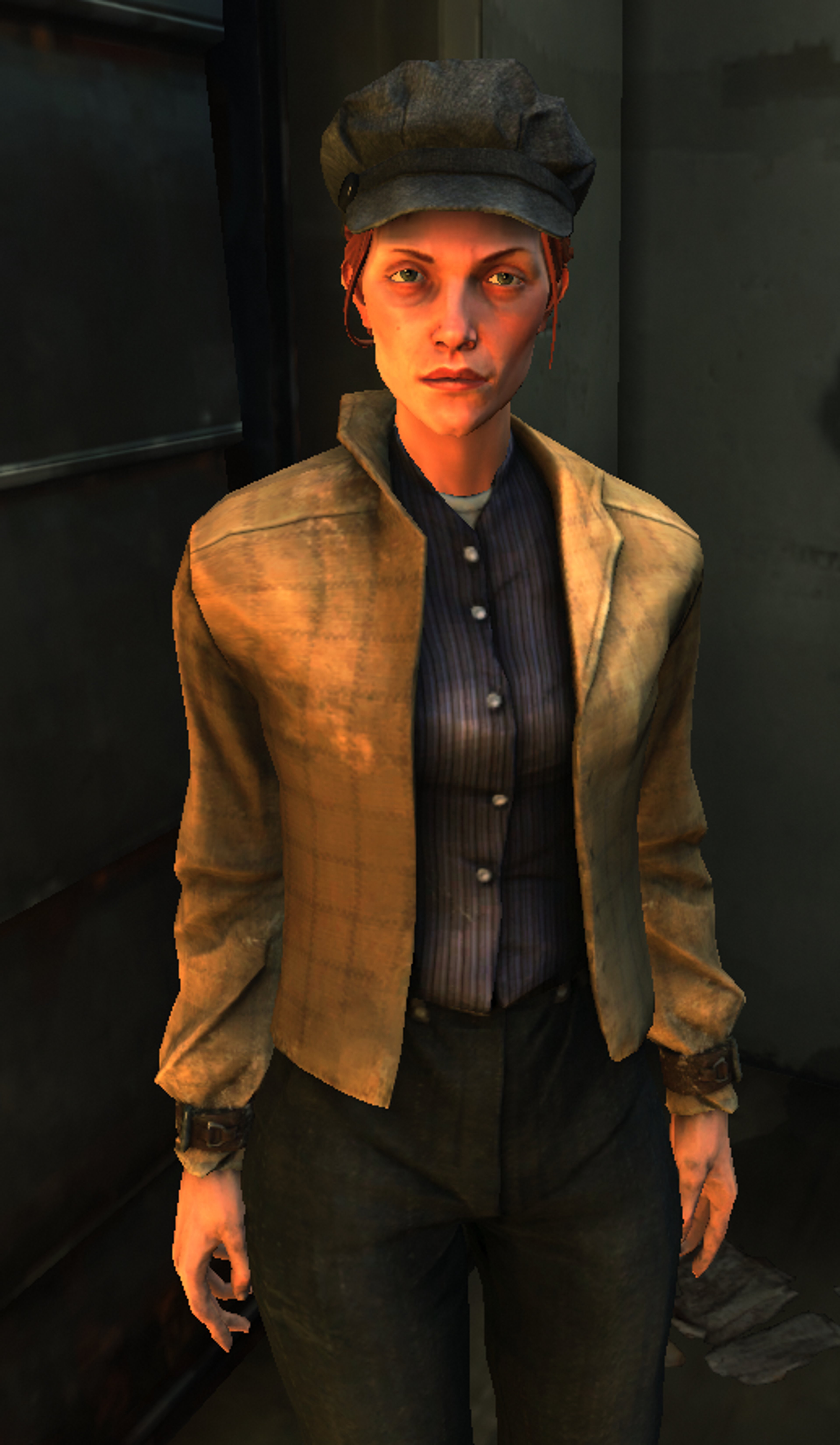 A young woman with short dark hair wearing a tan jacket and black shirt in a dimly lit indoor setting.