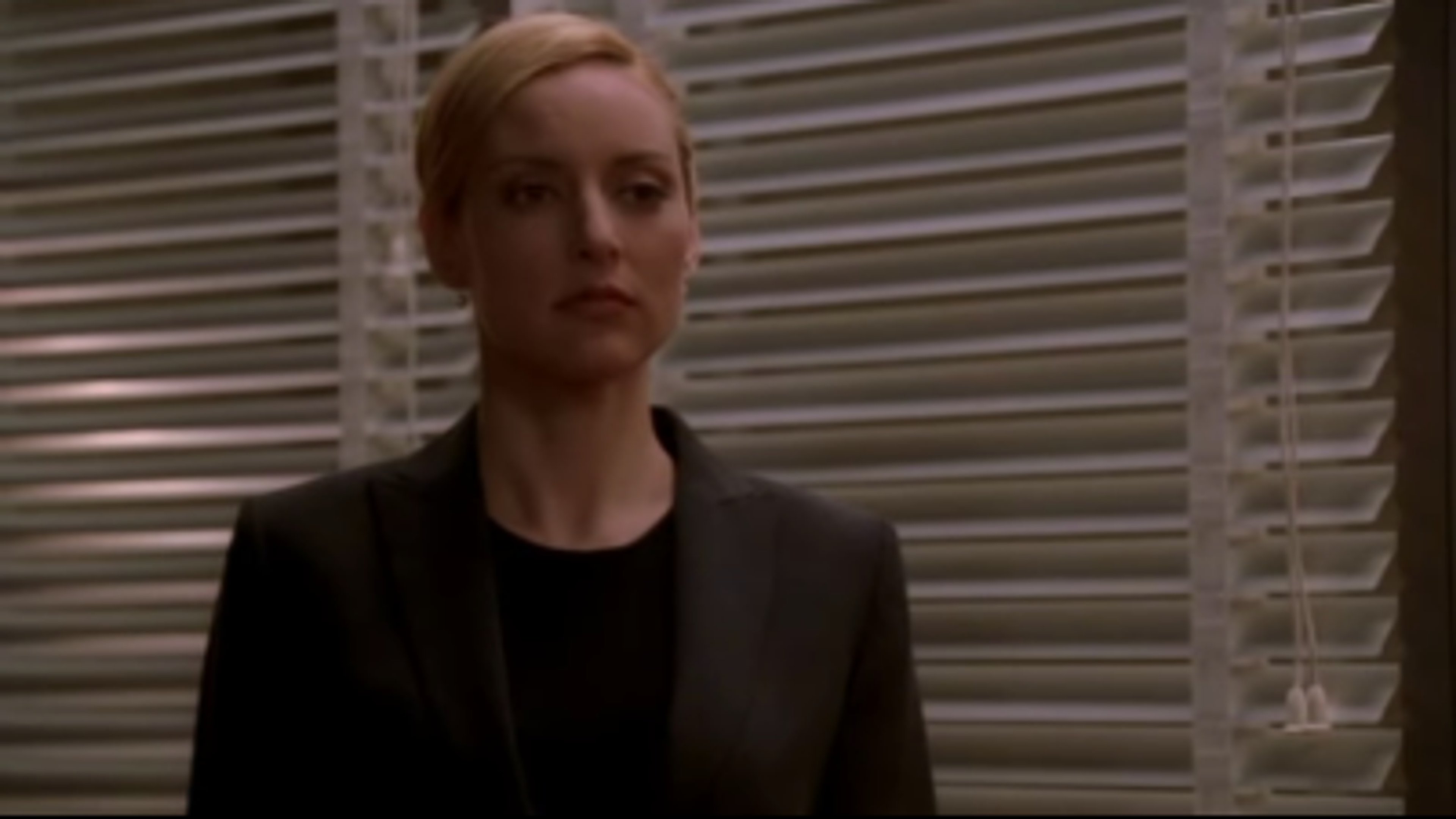 A woman with blonde hair wearing a black blazer in a dimly lit setting