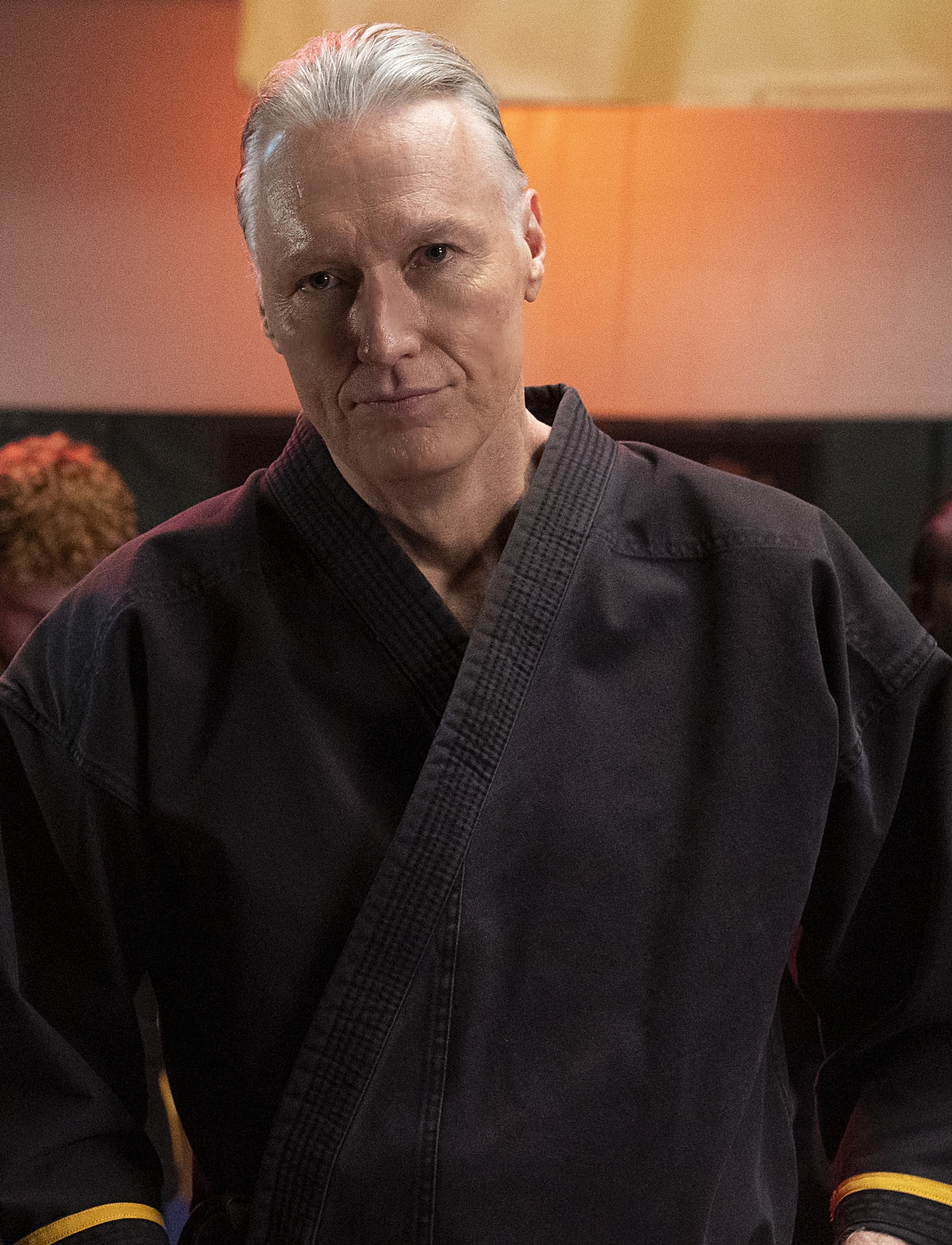 A man in a black martial arts uniform with a serious expression