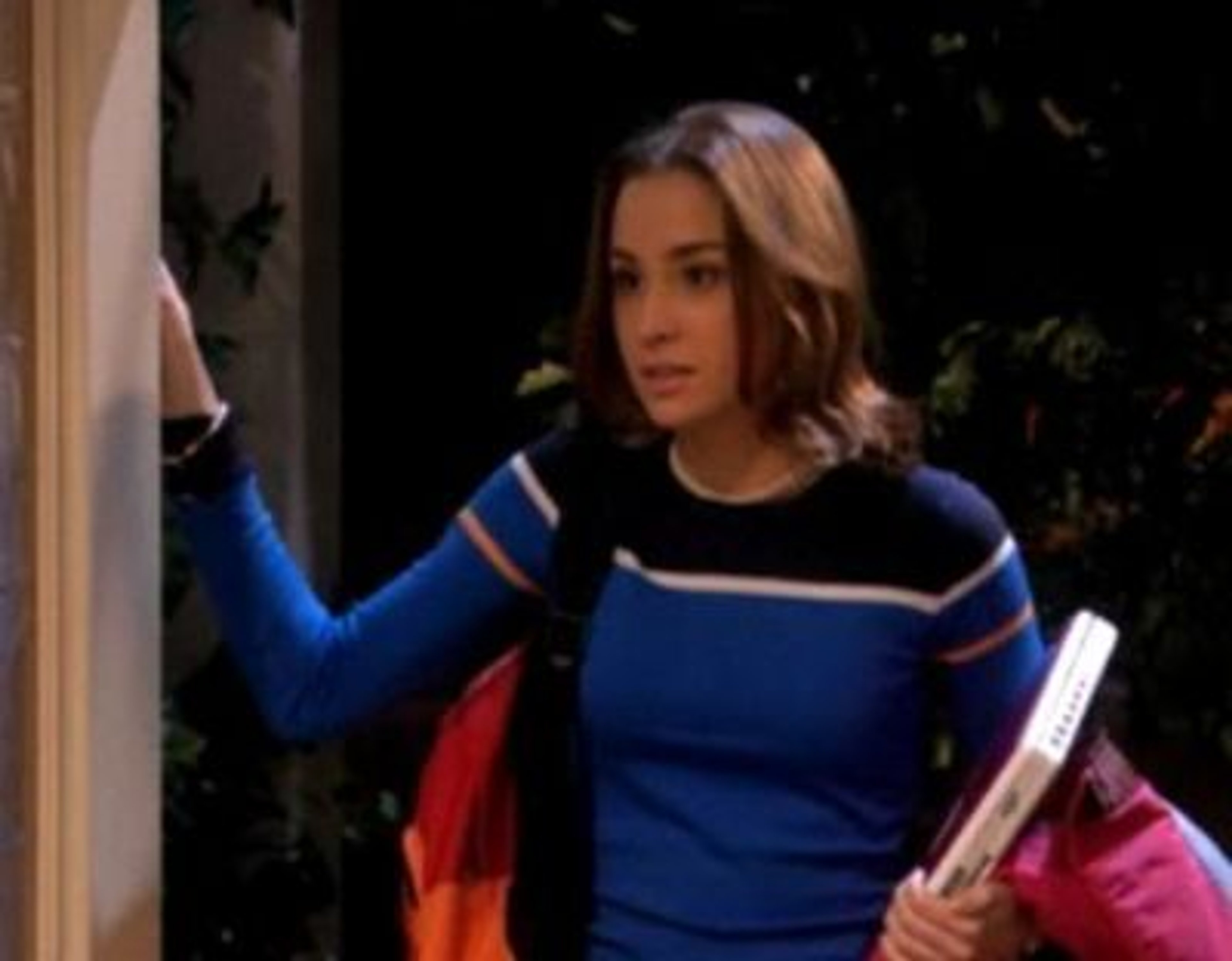 A young woman with long brown hair wearing a blue and white striped sweater, holding books and papers.