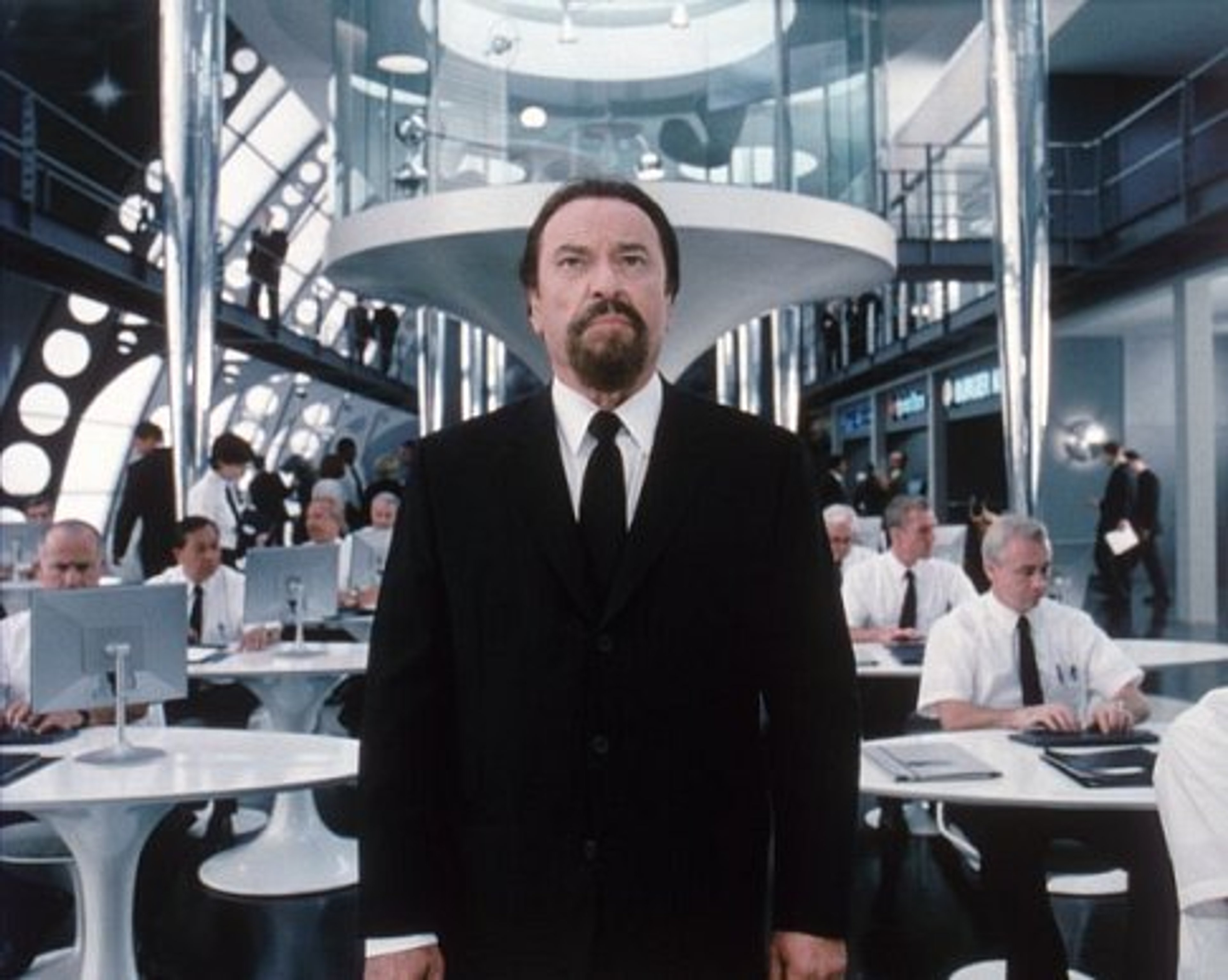 A serious-looking man in a suit standing in a high-tech environment