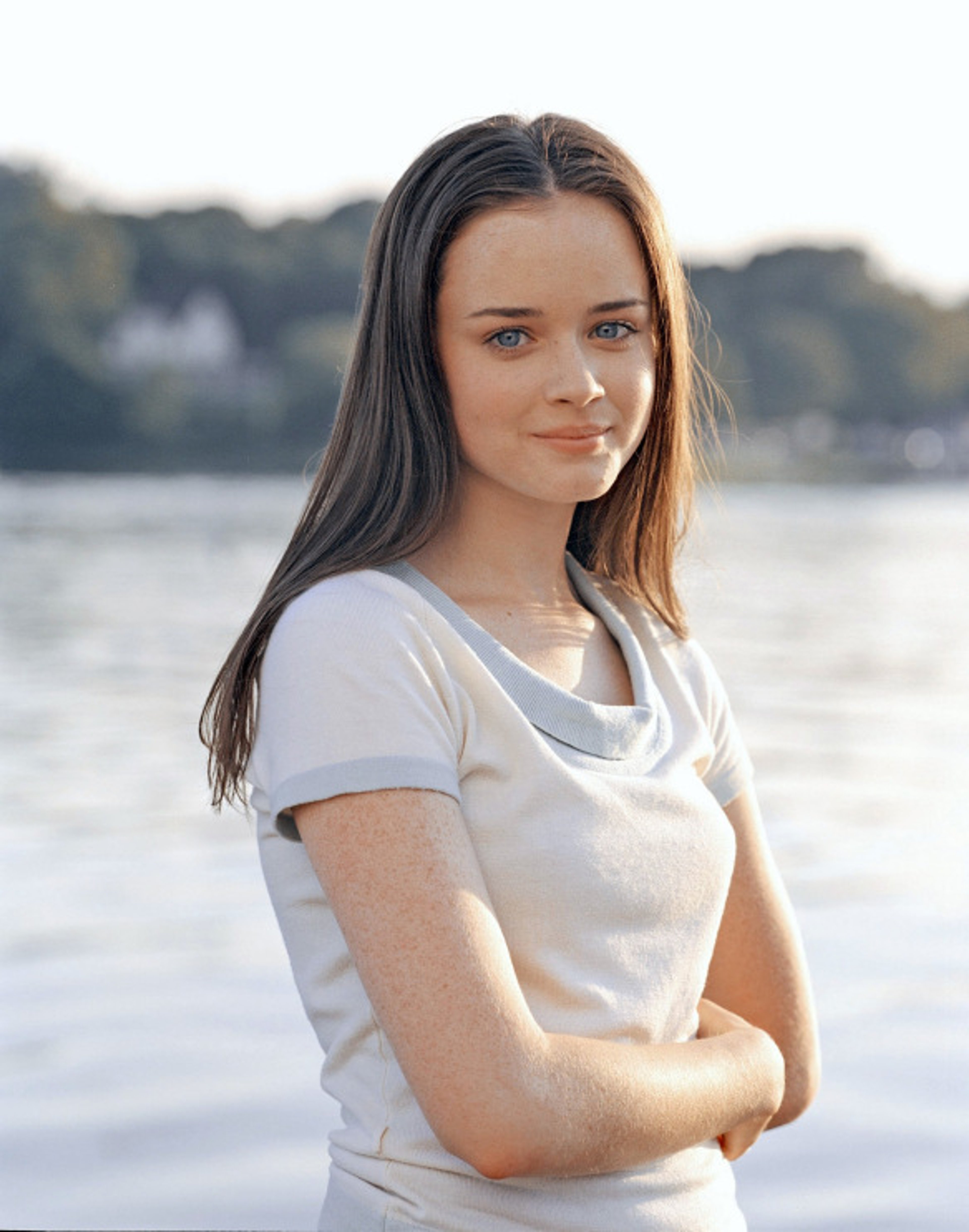 A young woman with long brown hair standing in front of a body of water