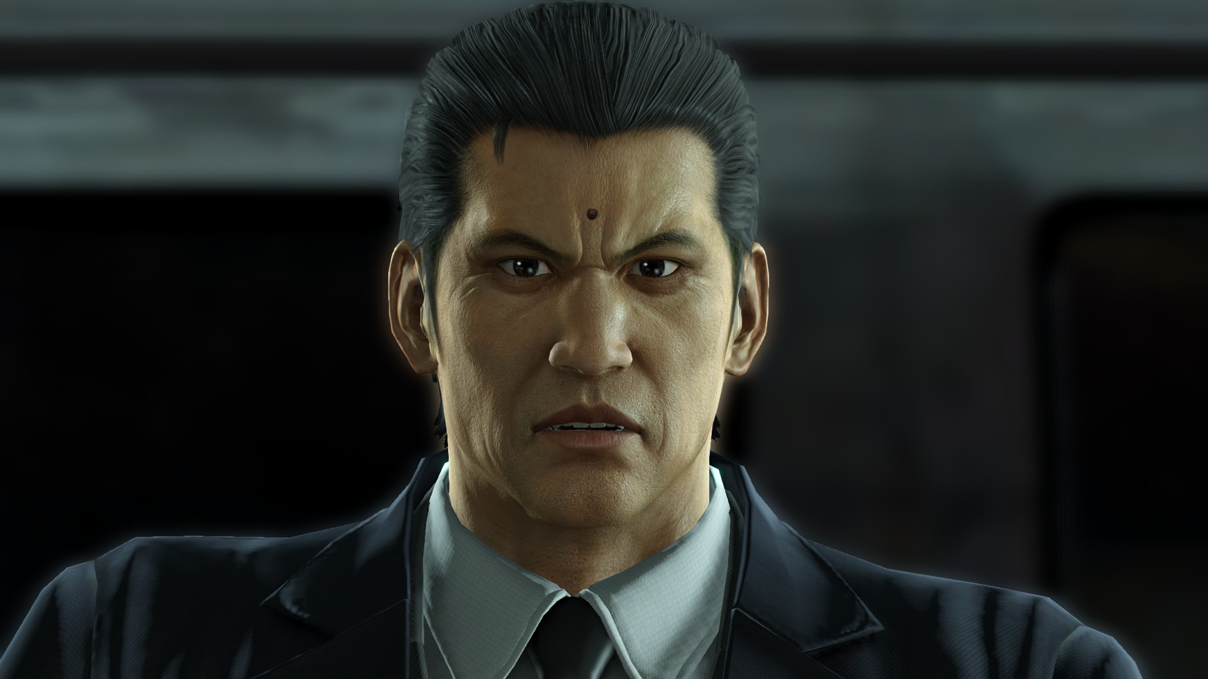 A middle-aged man in a suit with slicked-back graying hair and a mole on his forehead