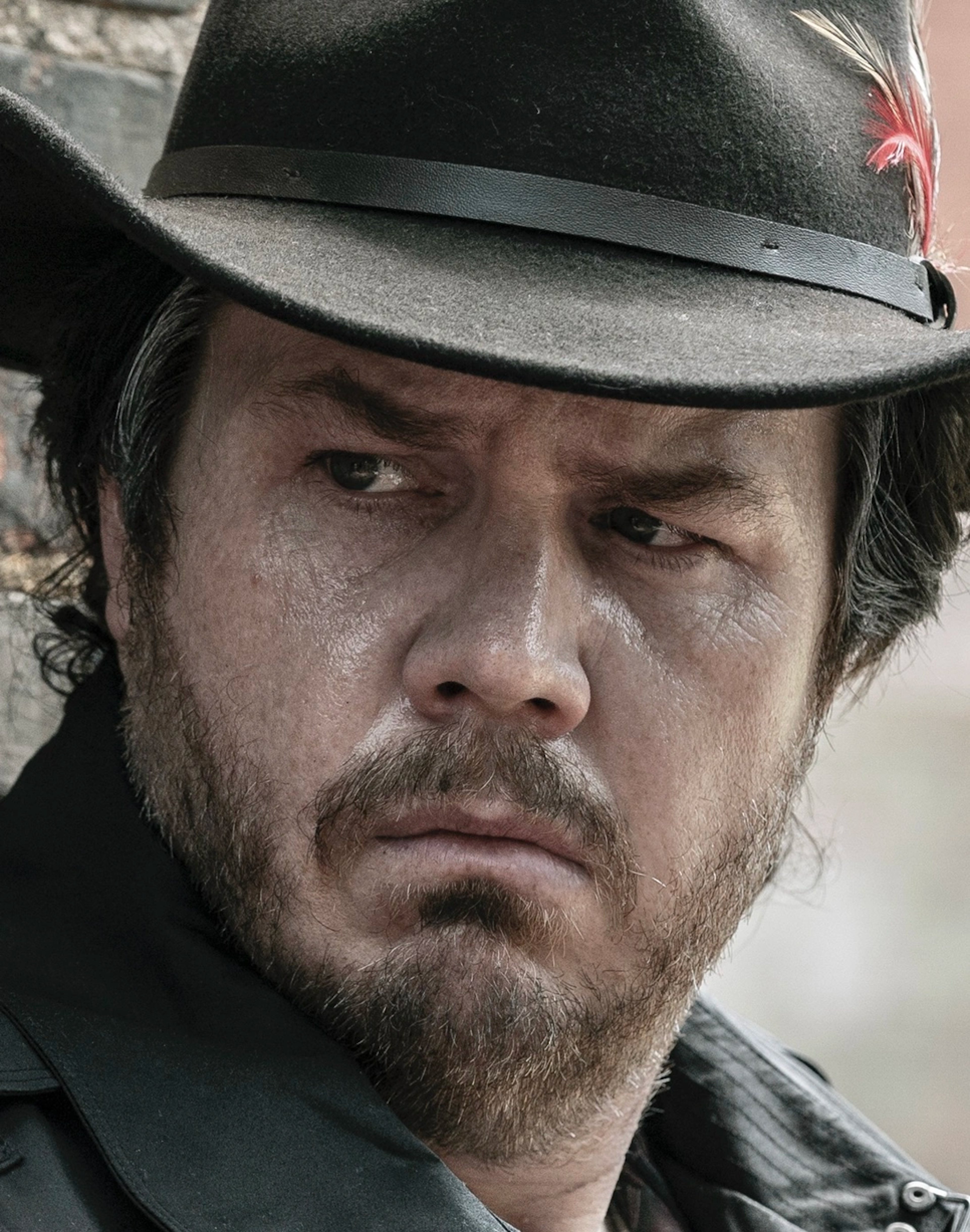 A middle-aged man with a beard wearing a black hat and jacket, looking serious.