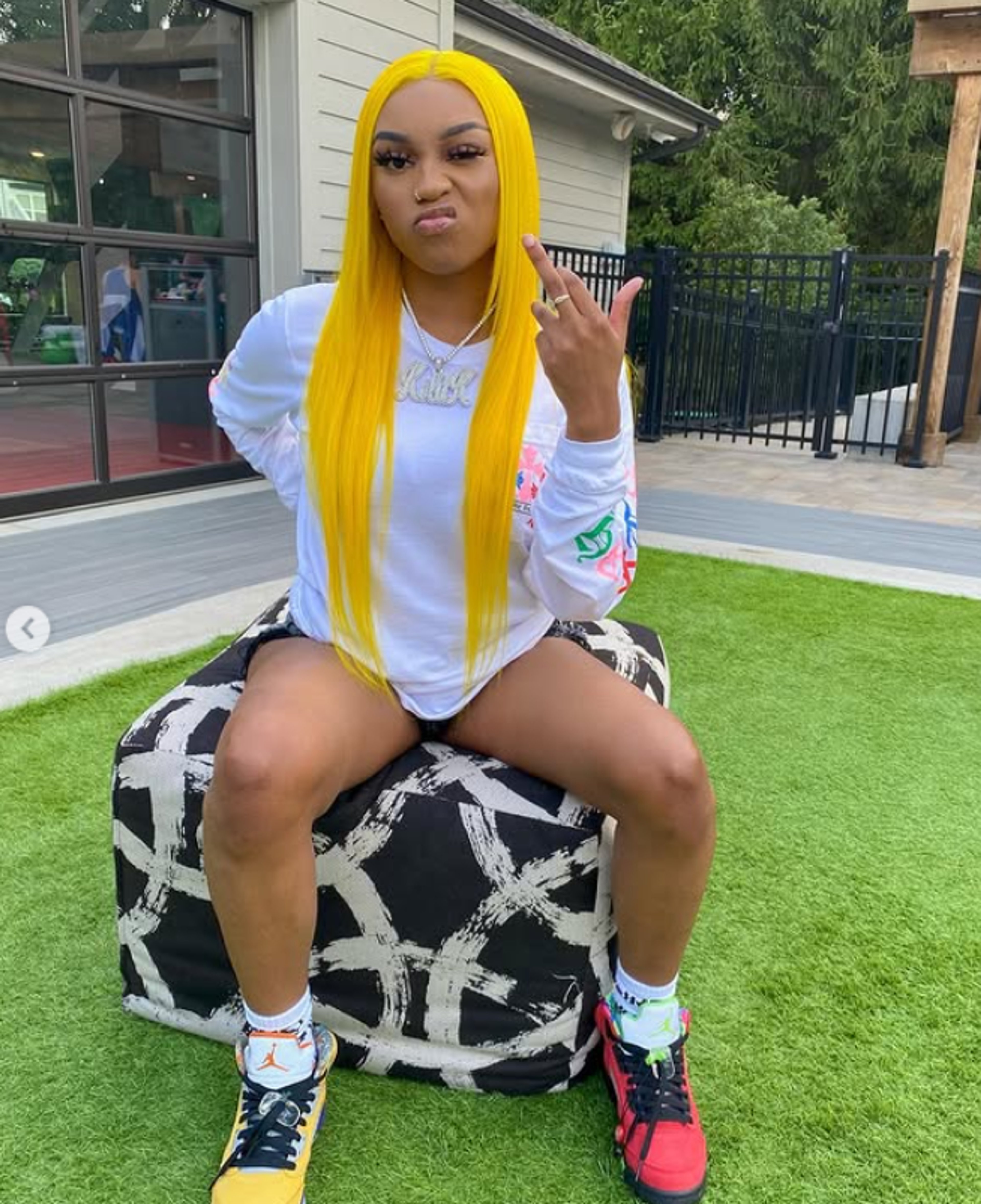 A young woman with bright yellow hair sitting on an inflatable chair or beanbag, wearing a white crop top and black shorts.